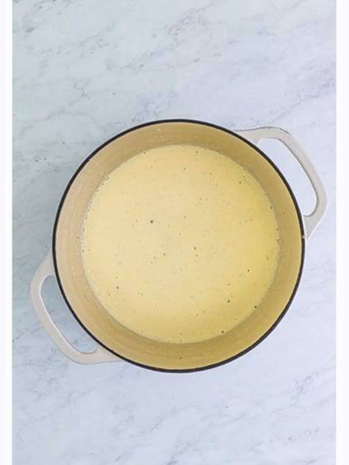 Creamy alfredo sauce whisked smooth in a pot.