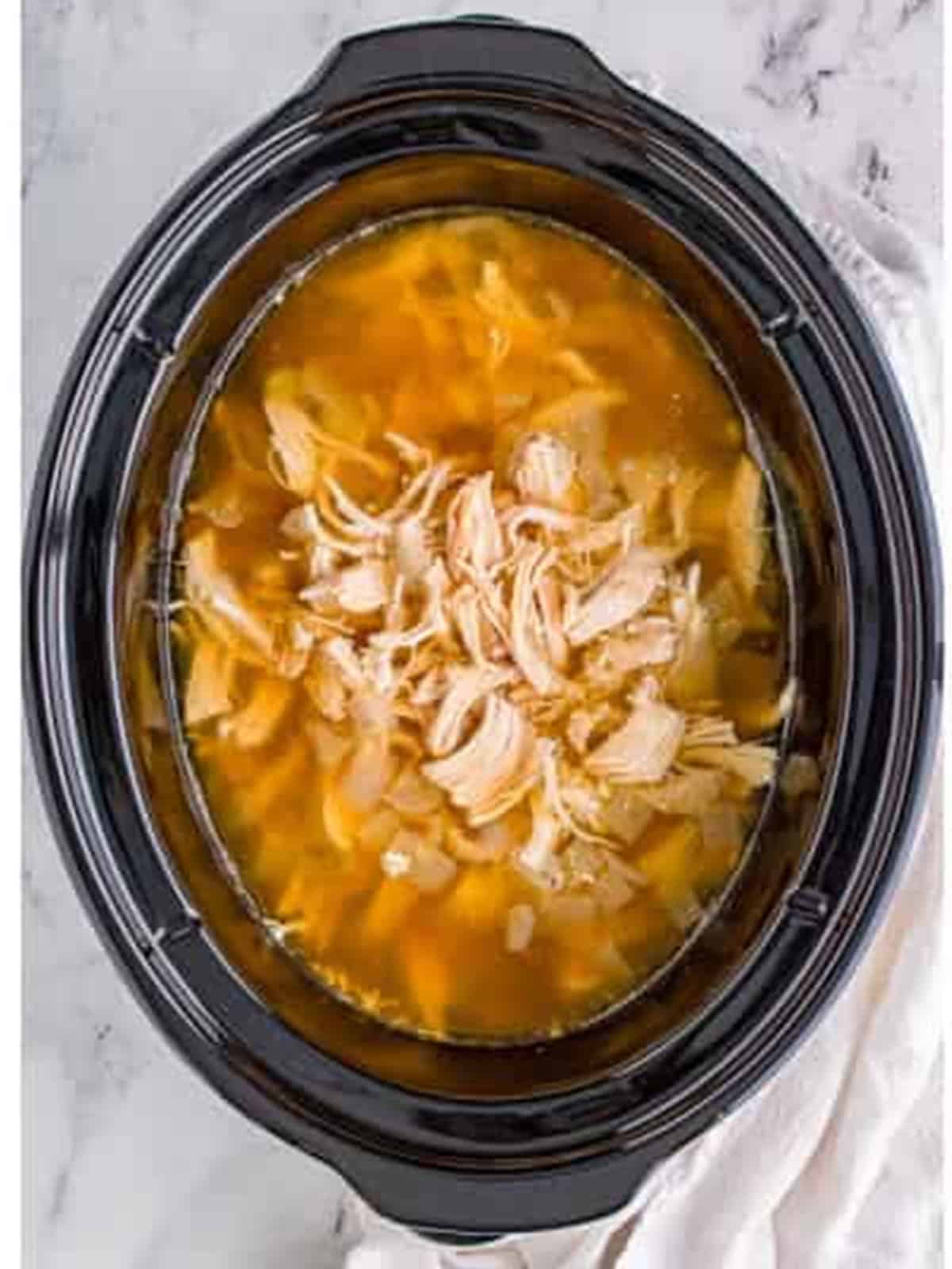 Shredded chicken stirred back into the slow cooker broth.