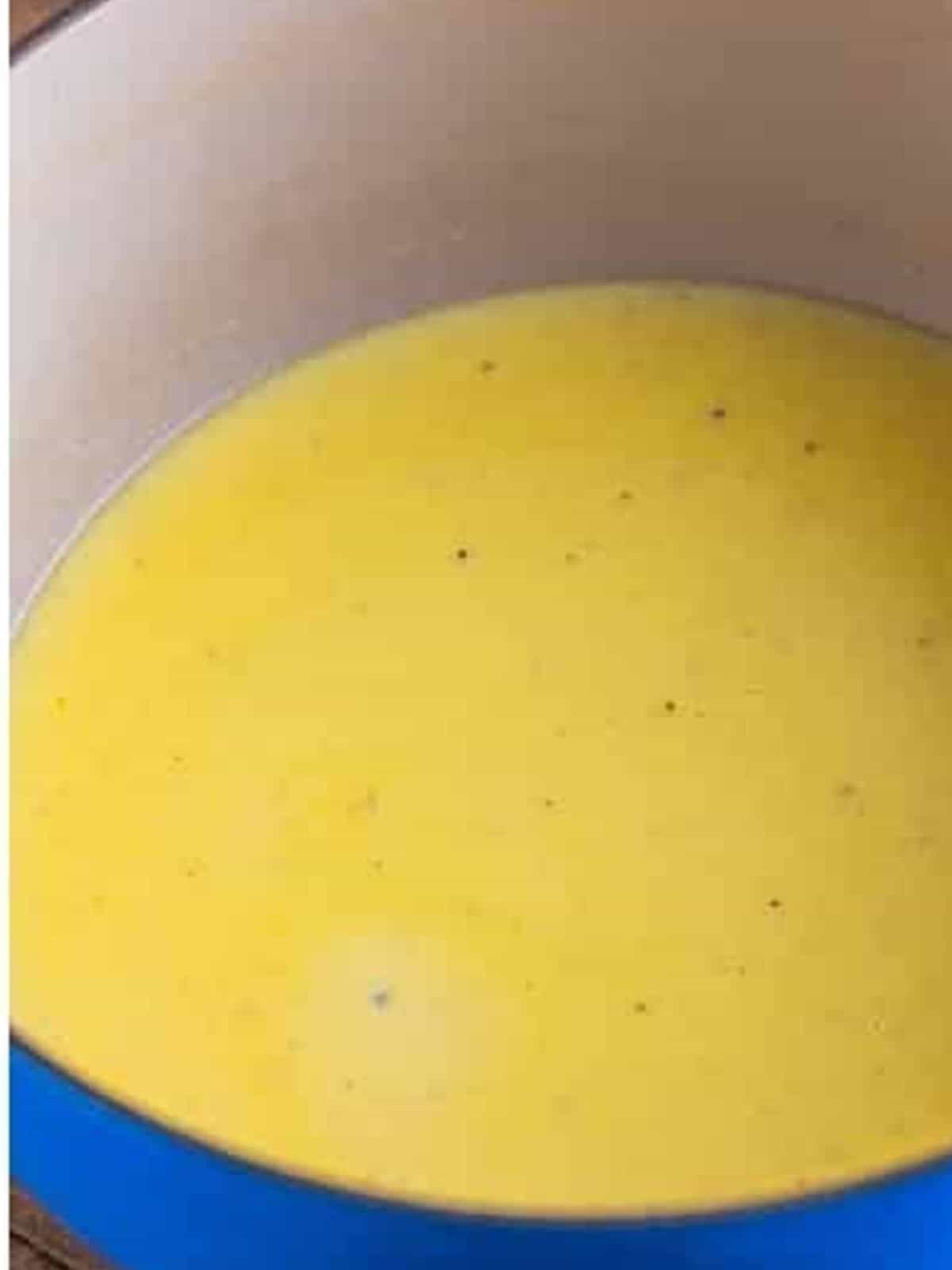 Whisking milk, chicken stock, and cream into the alfredo sauce until smooth.