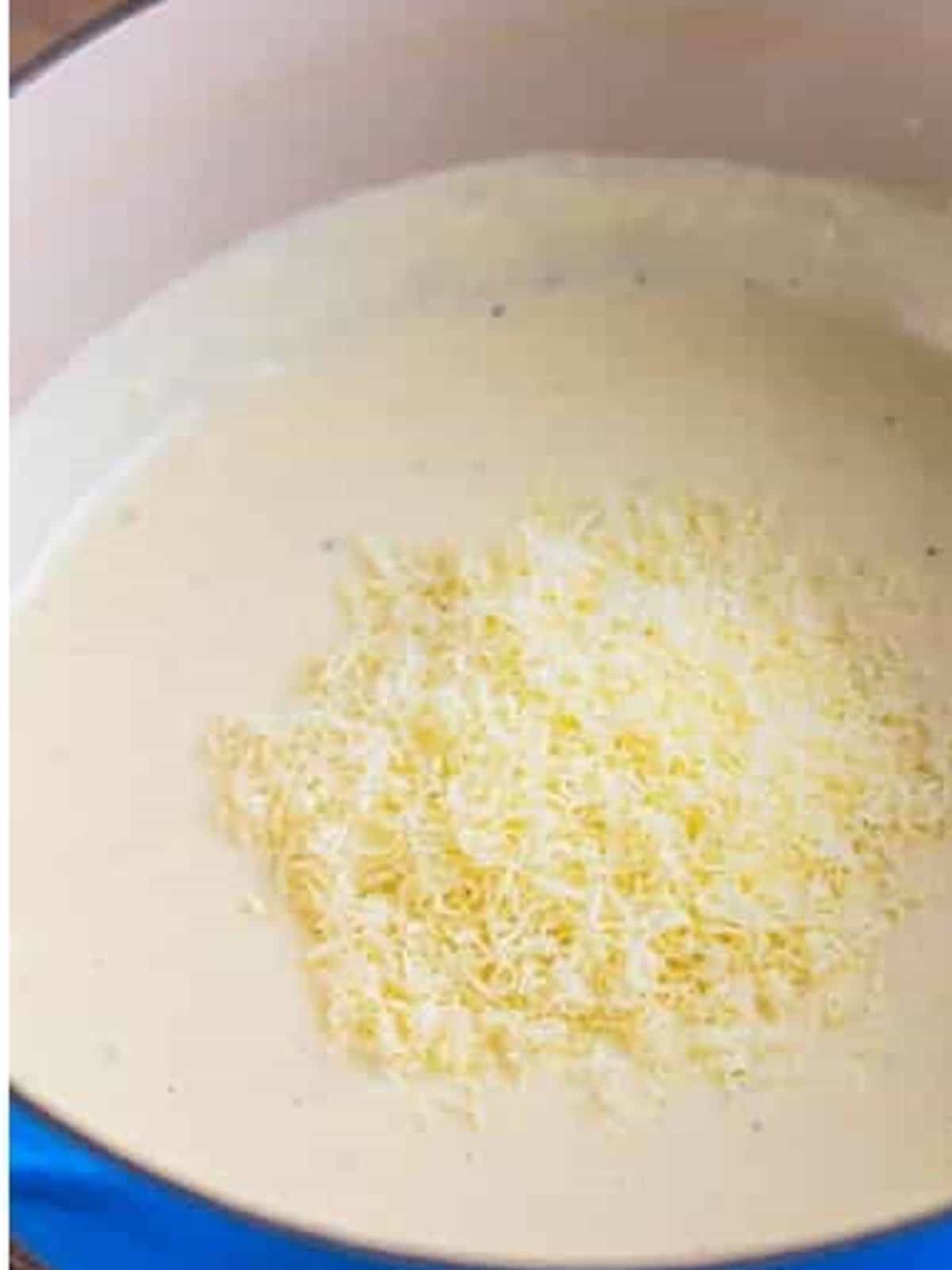 Stirring grated parmesan into the creamy alfredo sauce.