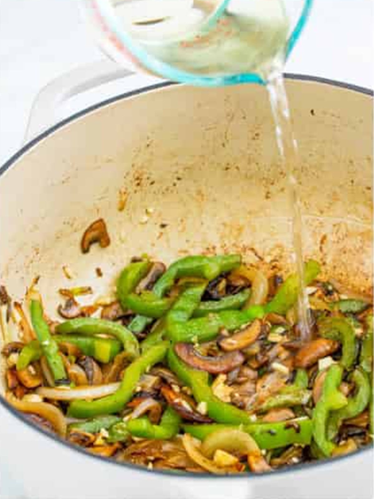 White wine being poured into the dutch oven to deglaze for chicken cacciatore.