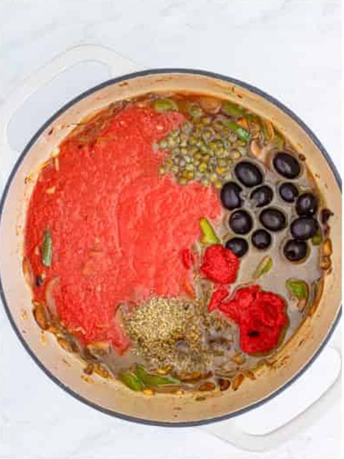 Crushed tomatoes, olives, capers, and Italian seasoning added to the dutch oven for chicken cacciatore.