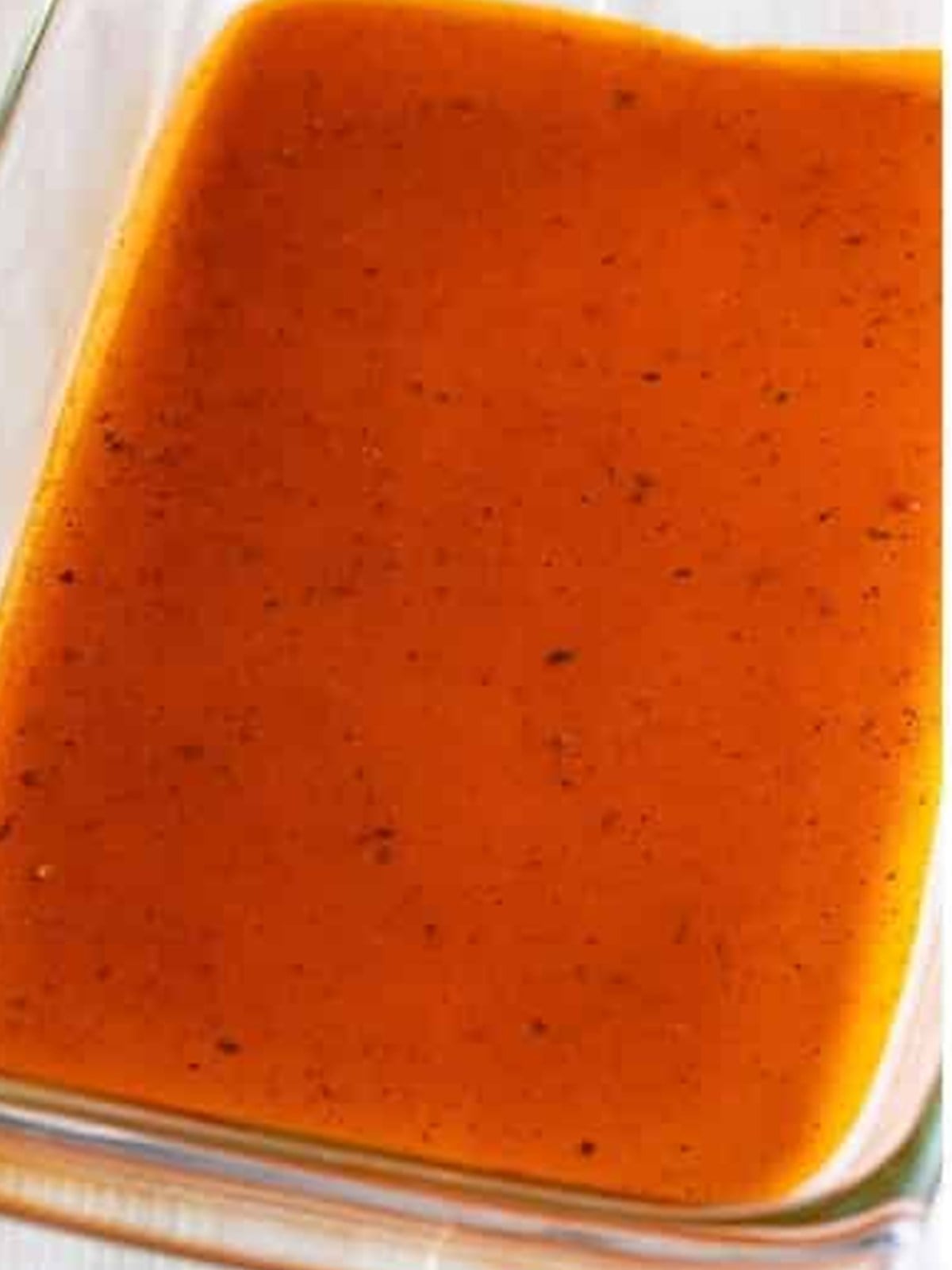 Enchilada sauce spread in the bottom of a baking dish.