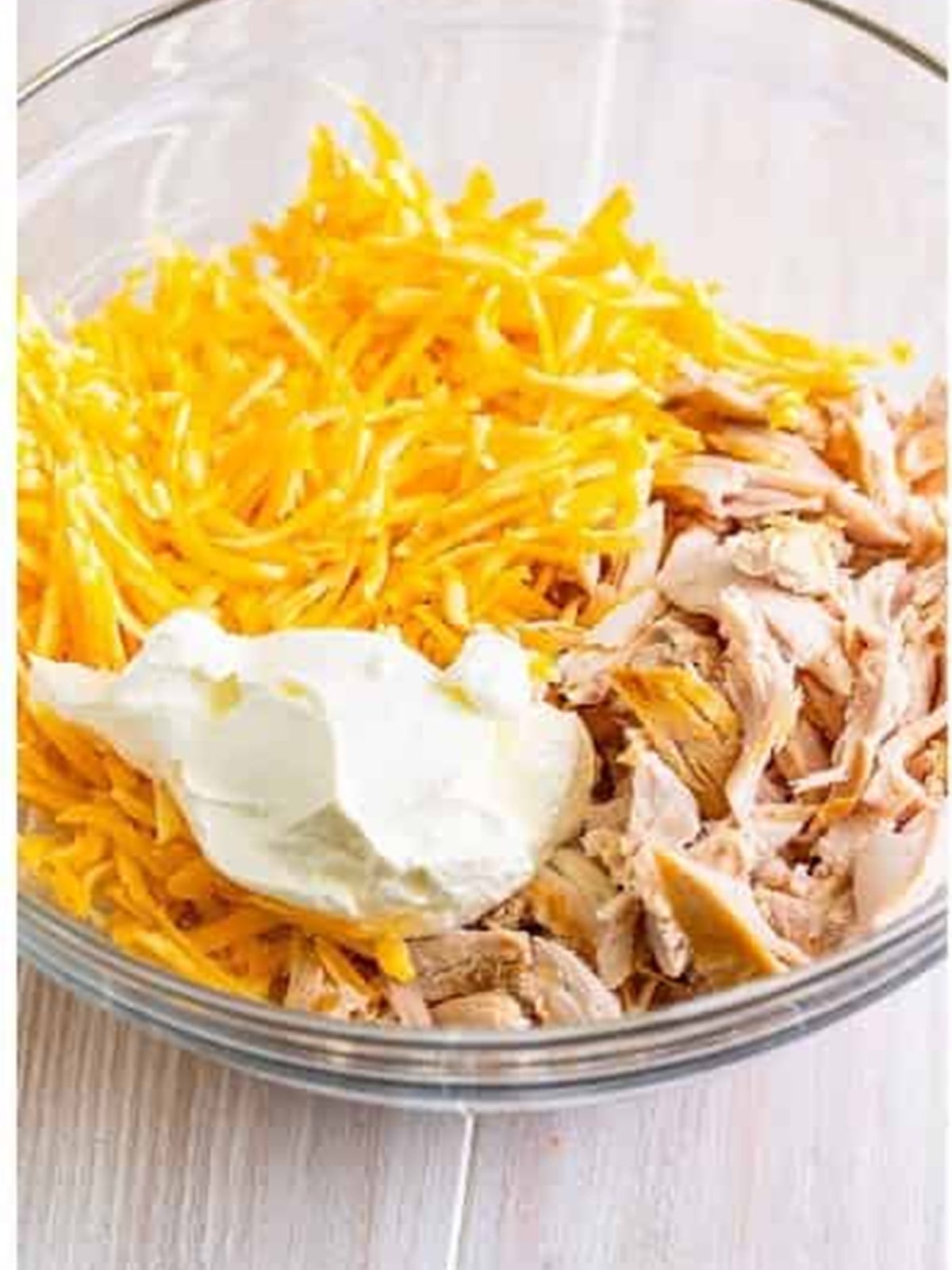 Shredded rotisserie chicken, colby jack cheese, and sour cream in a bowl for chicken enchiladas filling.