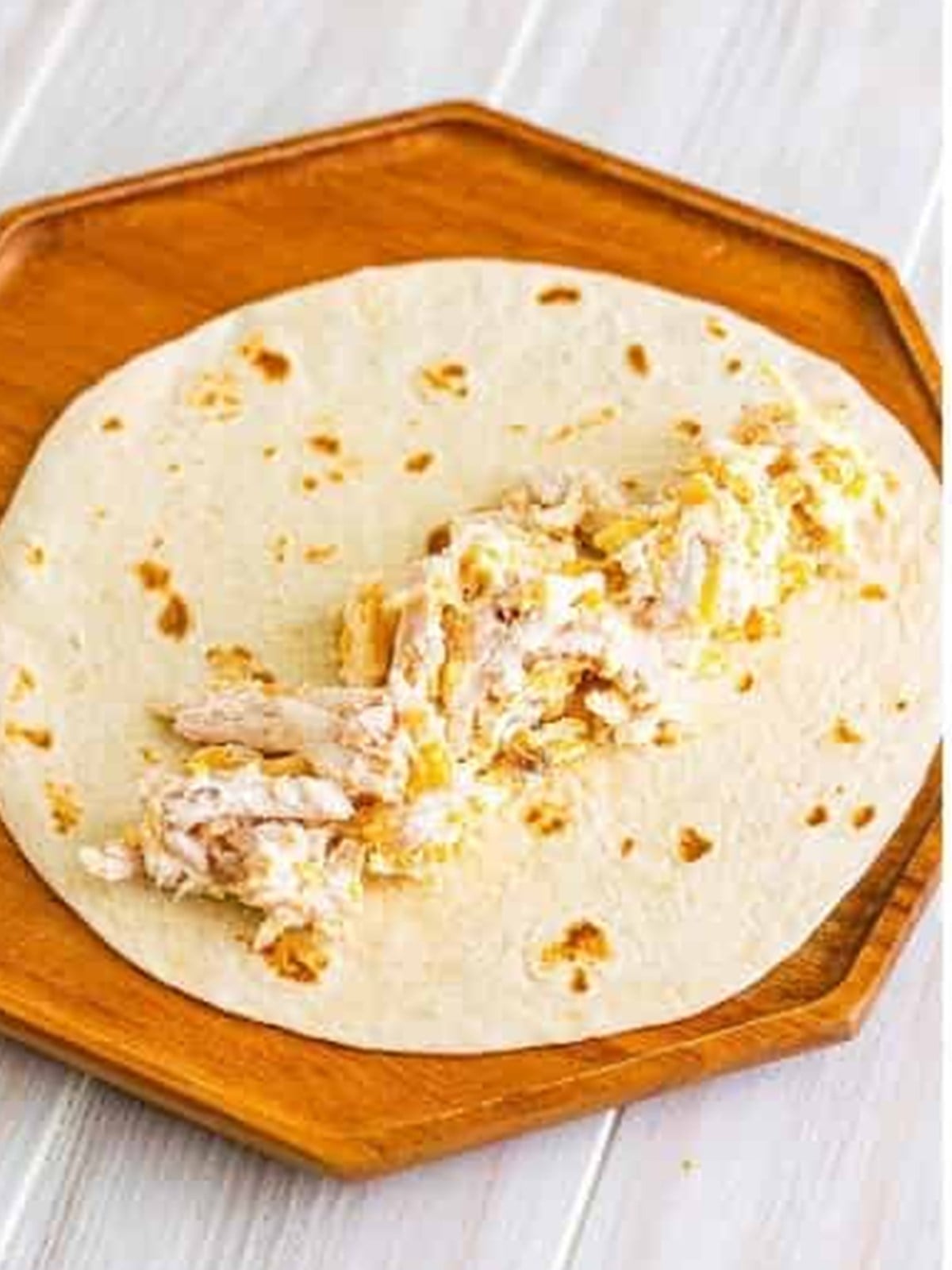 Rotisserie chicken filling spooned onto a soft tortilla before rolling.