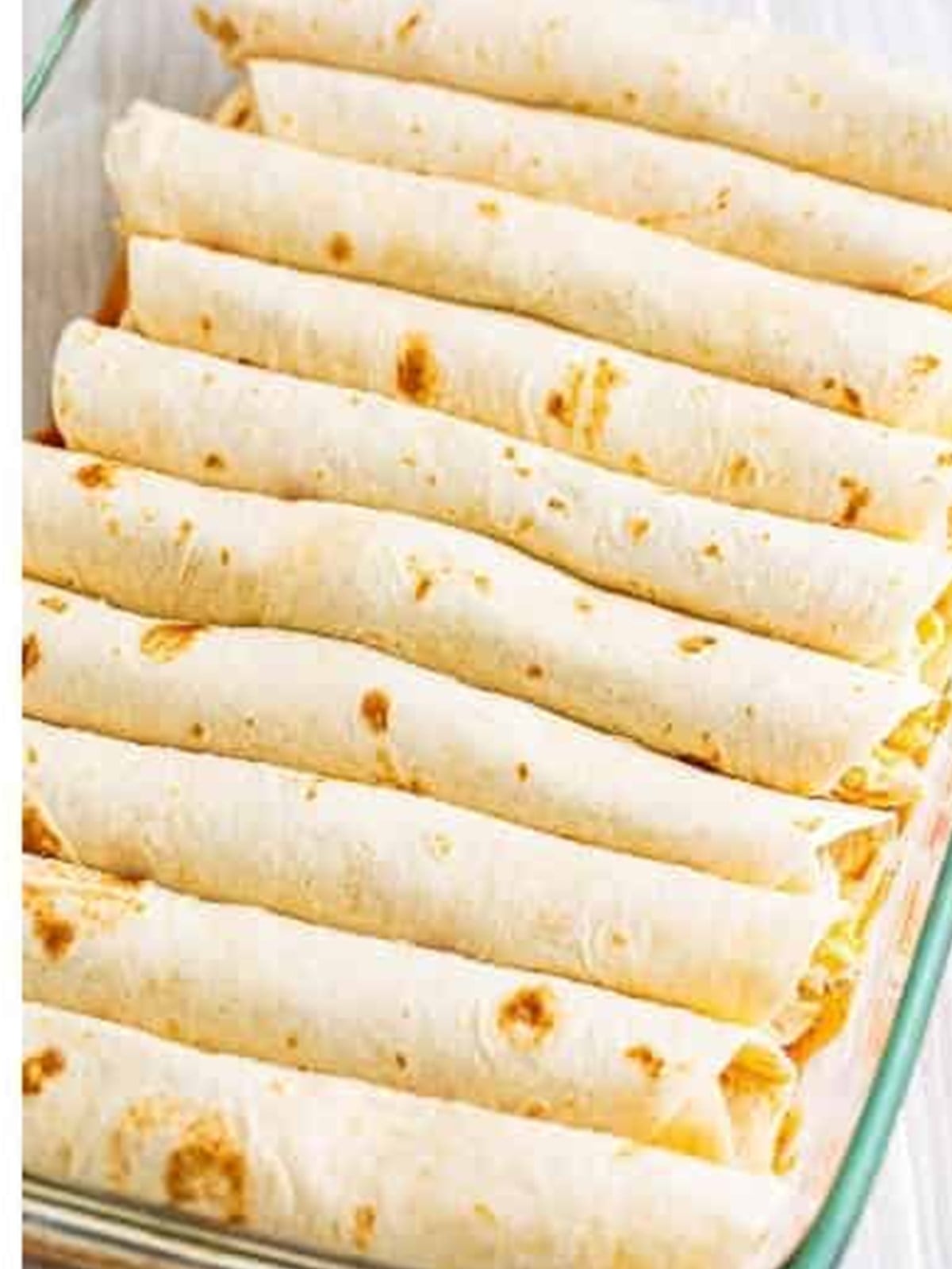 Rolled chicken enchiladas arranged seam side down in a baking dish.
