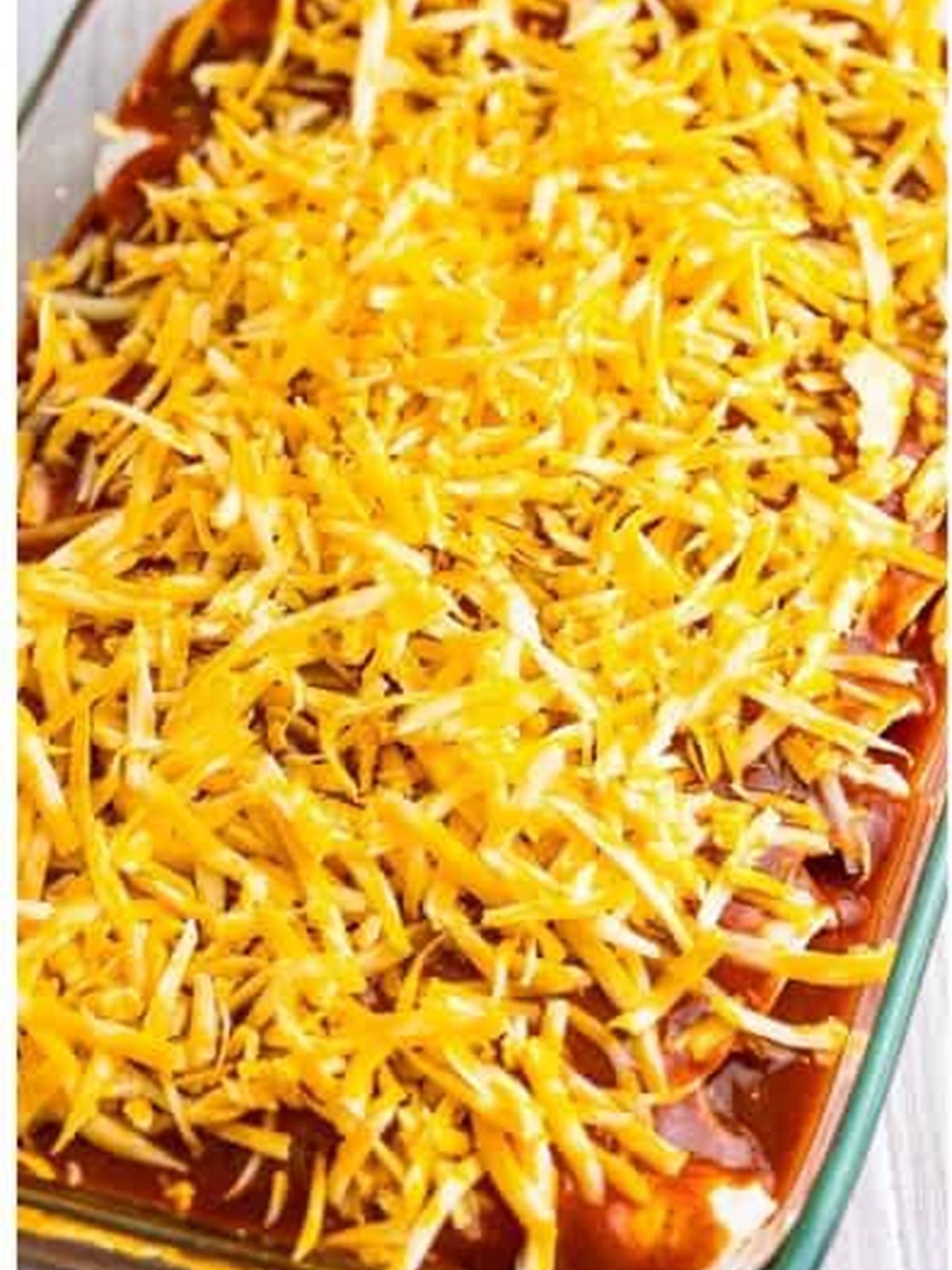 Chicken enchiladas topped with sauce and shredded cheese before baking.