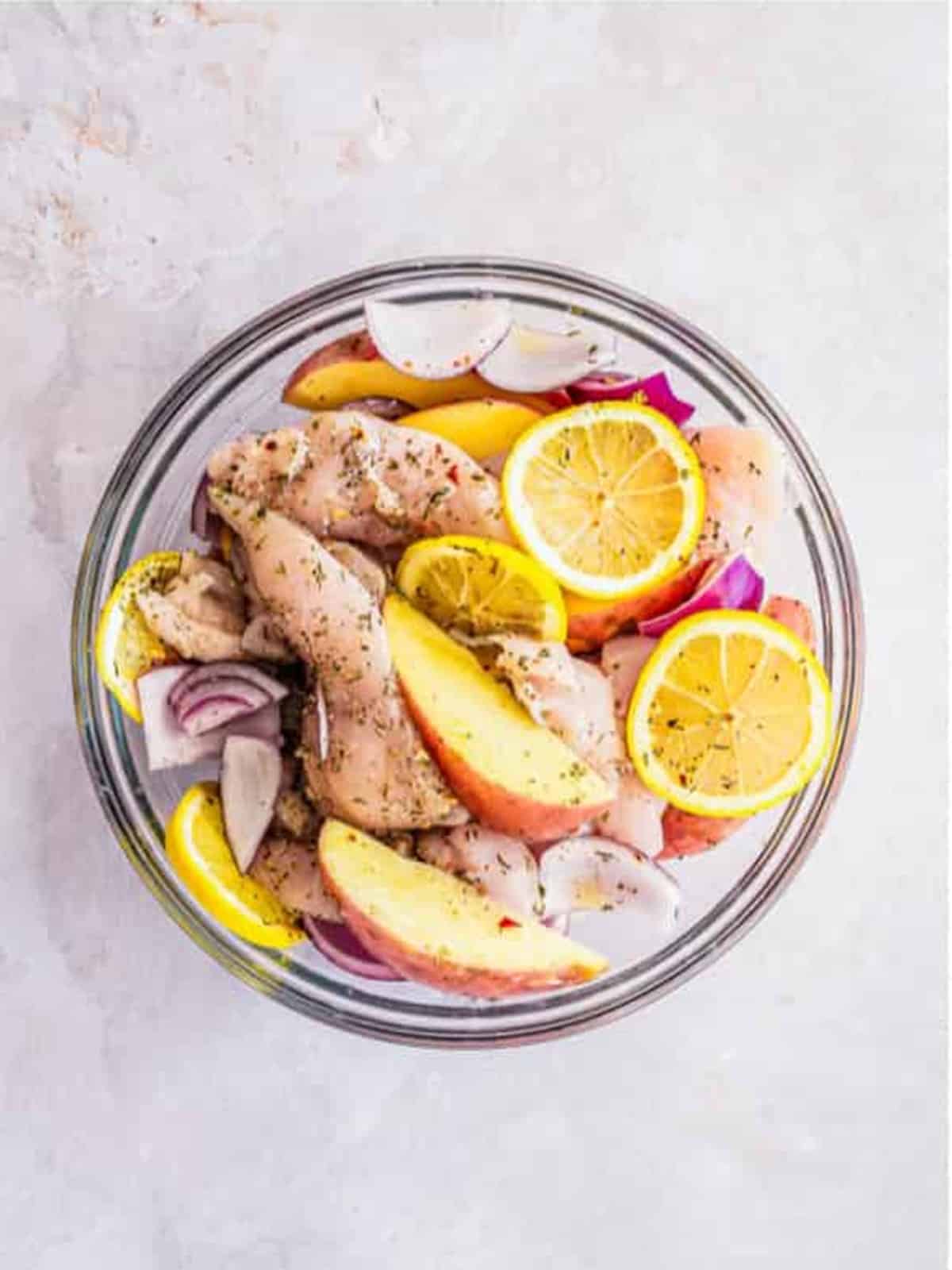 The chicken and potatoes coated in lemon juice, garlic, and Italian seasonings in the bowl.
