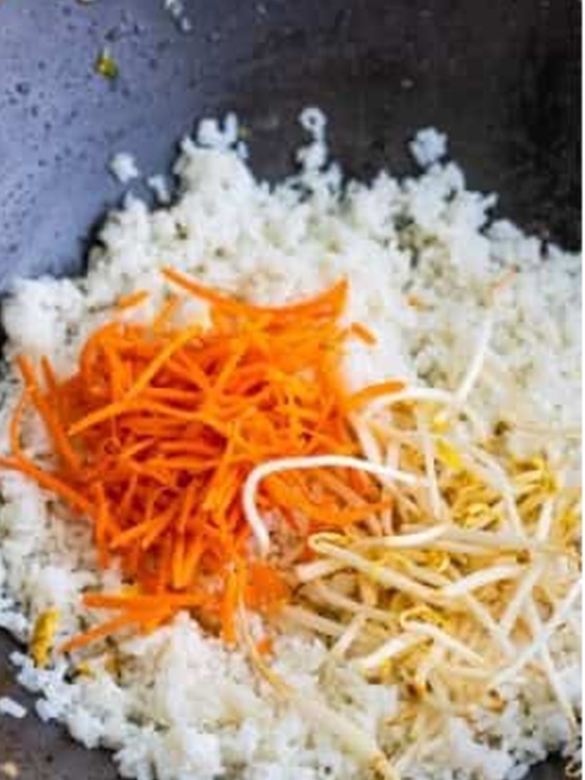 Cooked rice, shredded carrots, and bean sprouts added to a wok