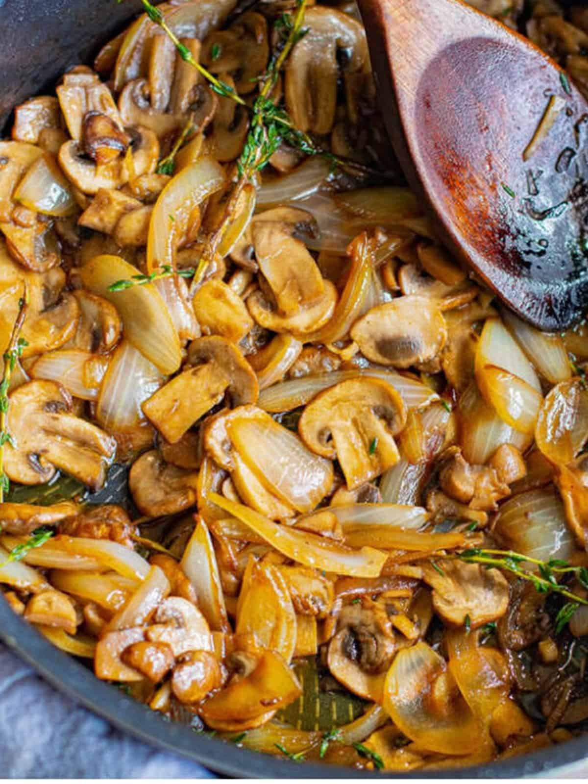 Sliced onions, garlic, thyme, and mushrooms cooking in a skillet.