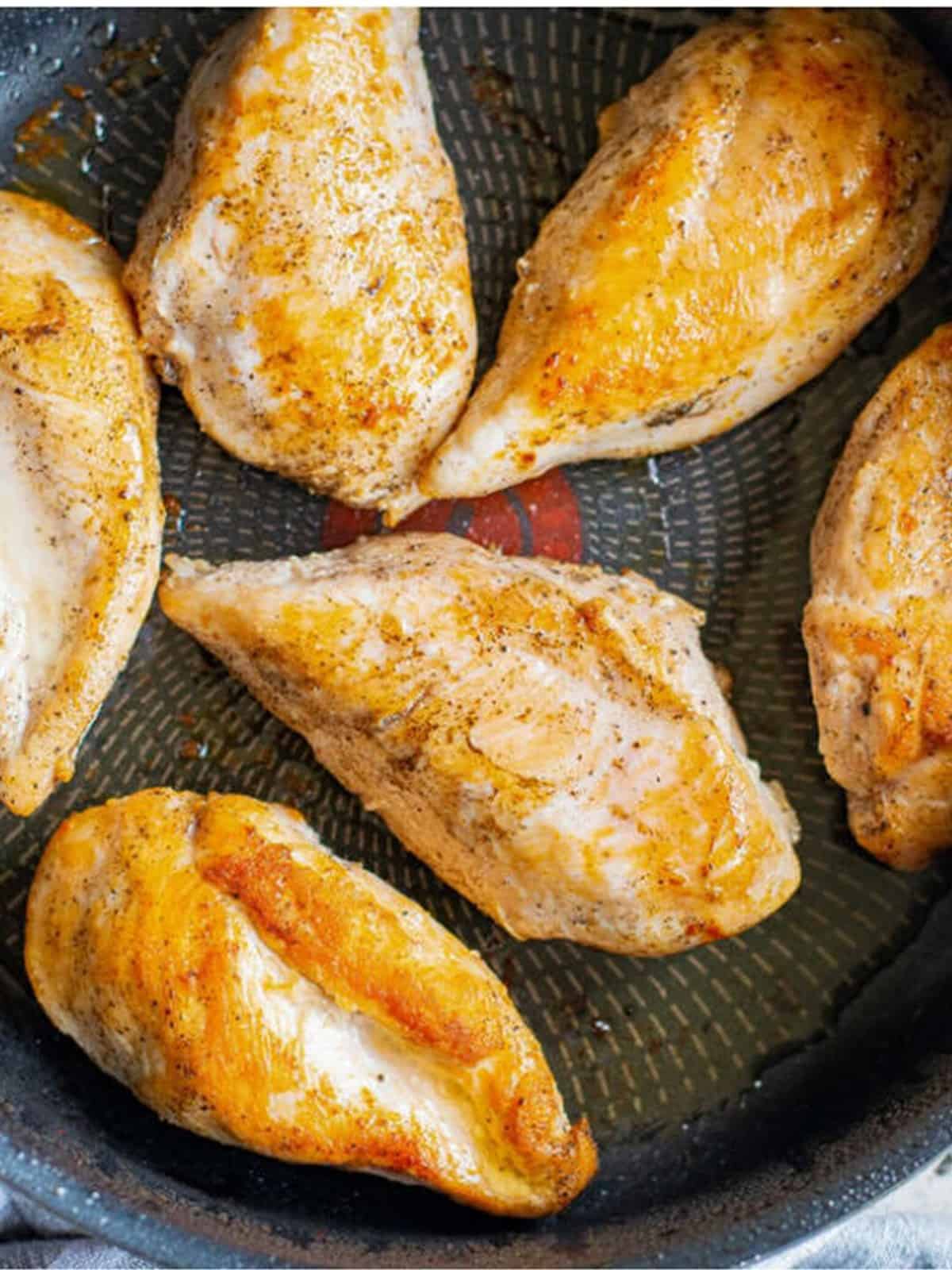 Chicken breasts browning in a skillet with olive oil.