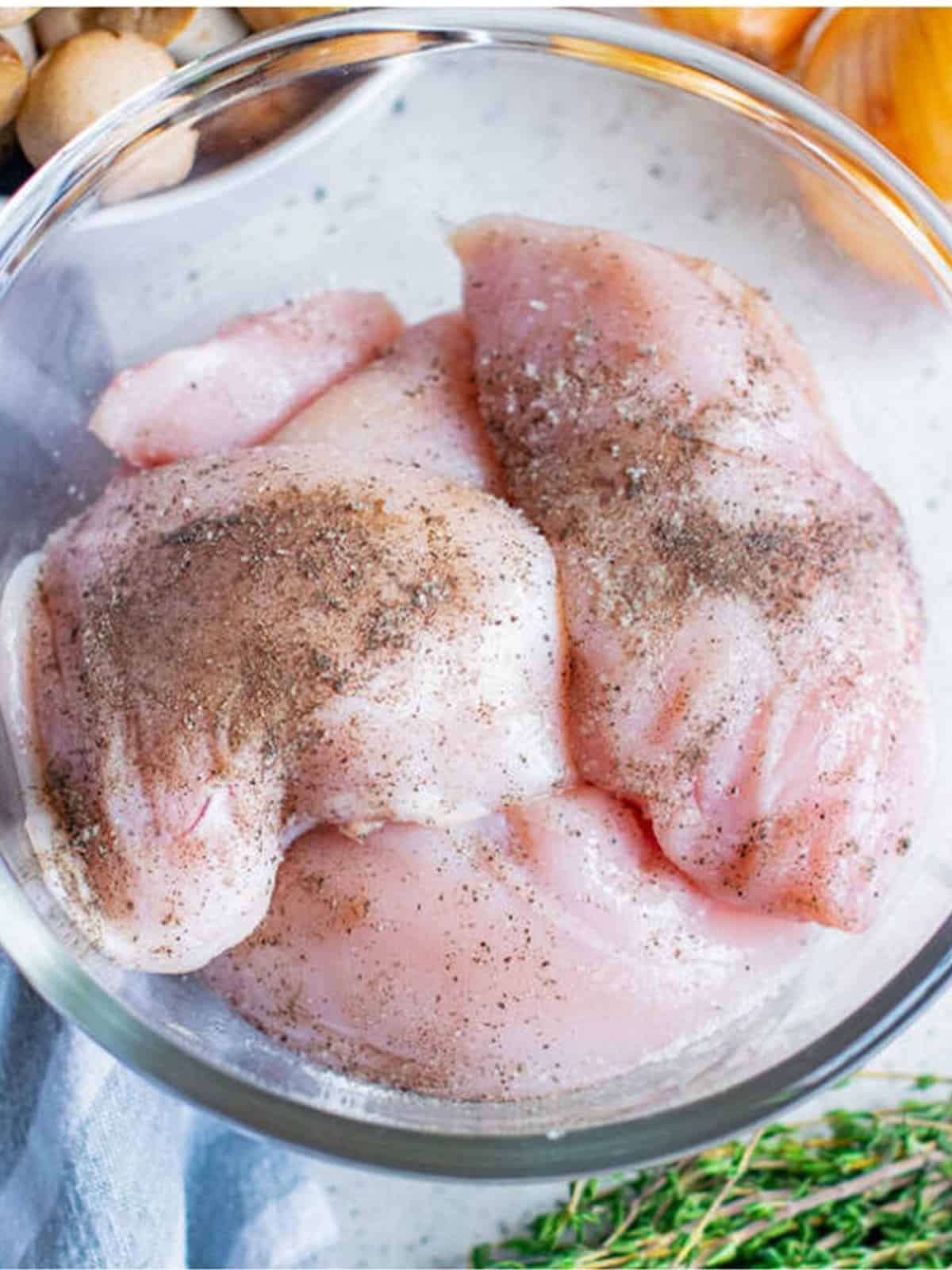 Raw chicken breasts seasoned with salt and pepper in a bowl.