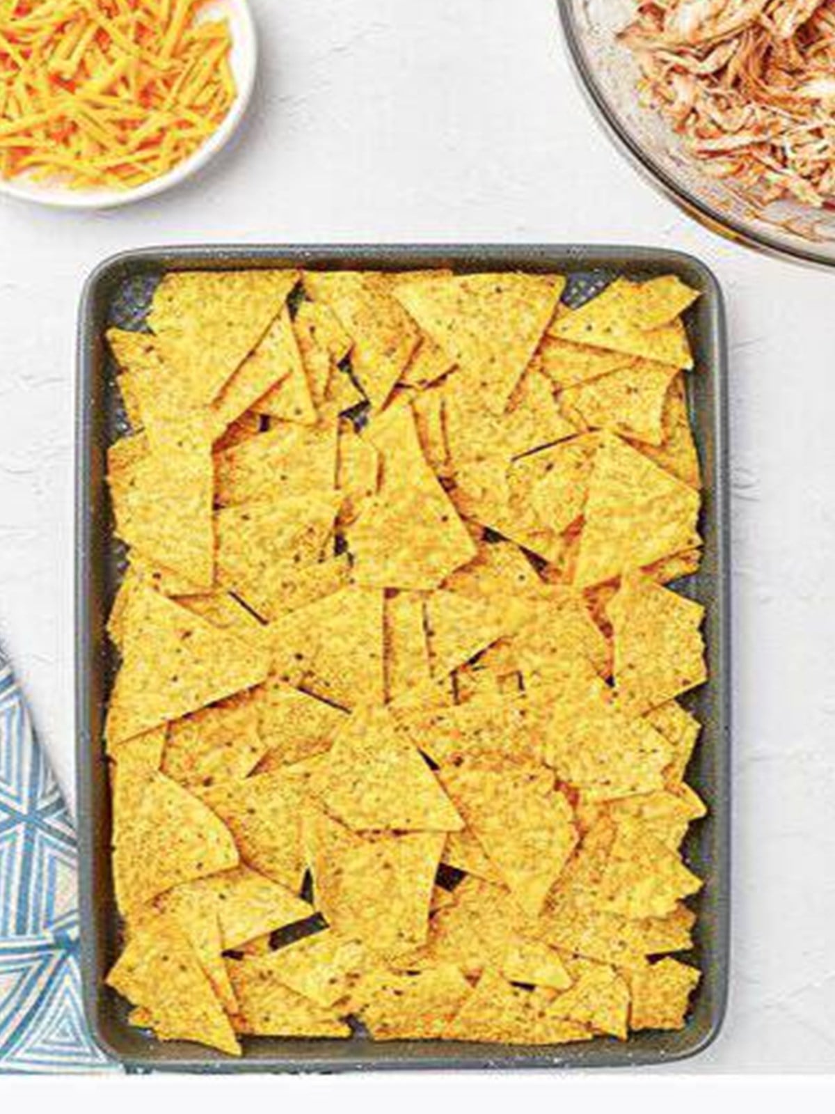 Tortilla chips spread in a single layer on a sheet tray.