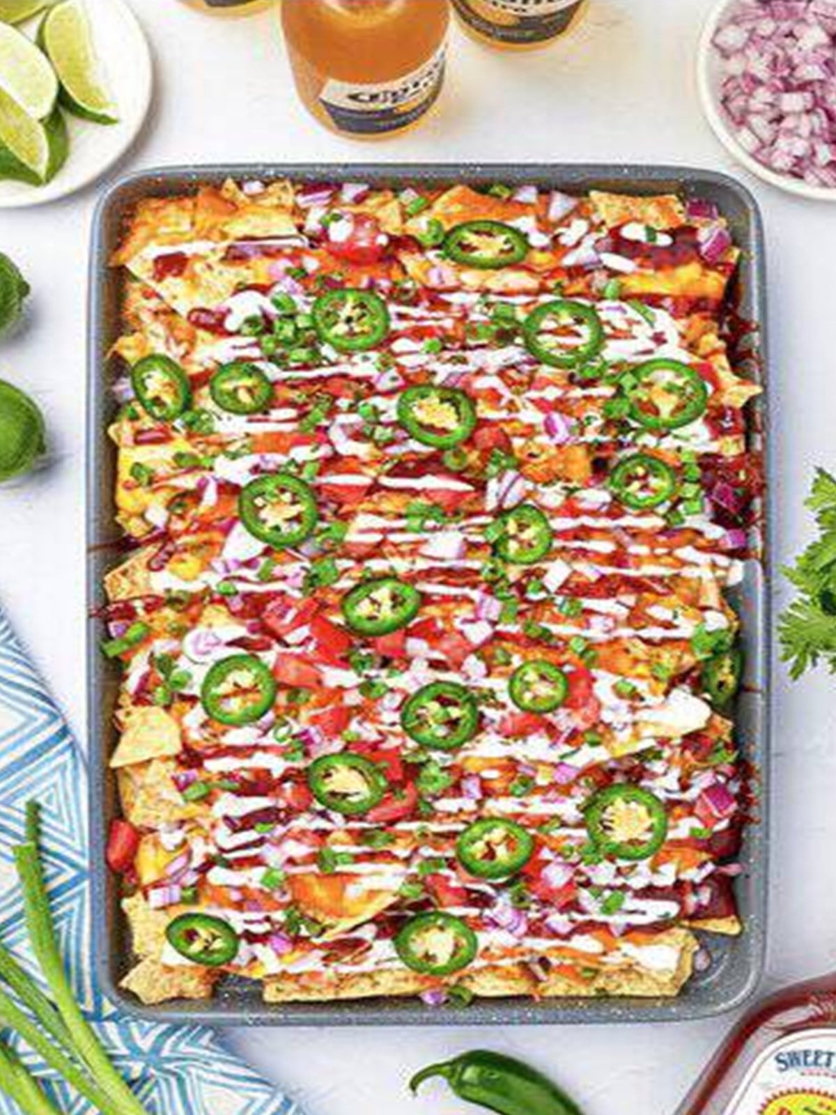 Loaded BBQ chicken nachos baked and topped with tomatoes, jalapenos, and sour cream.