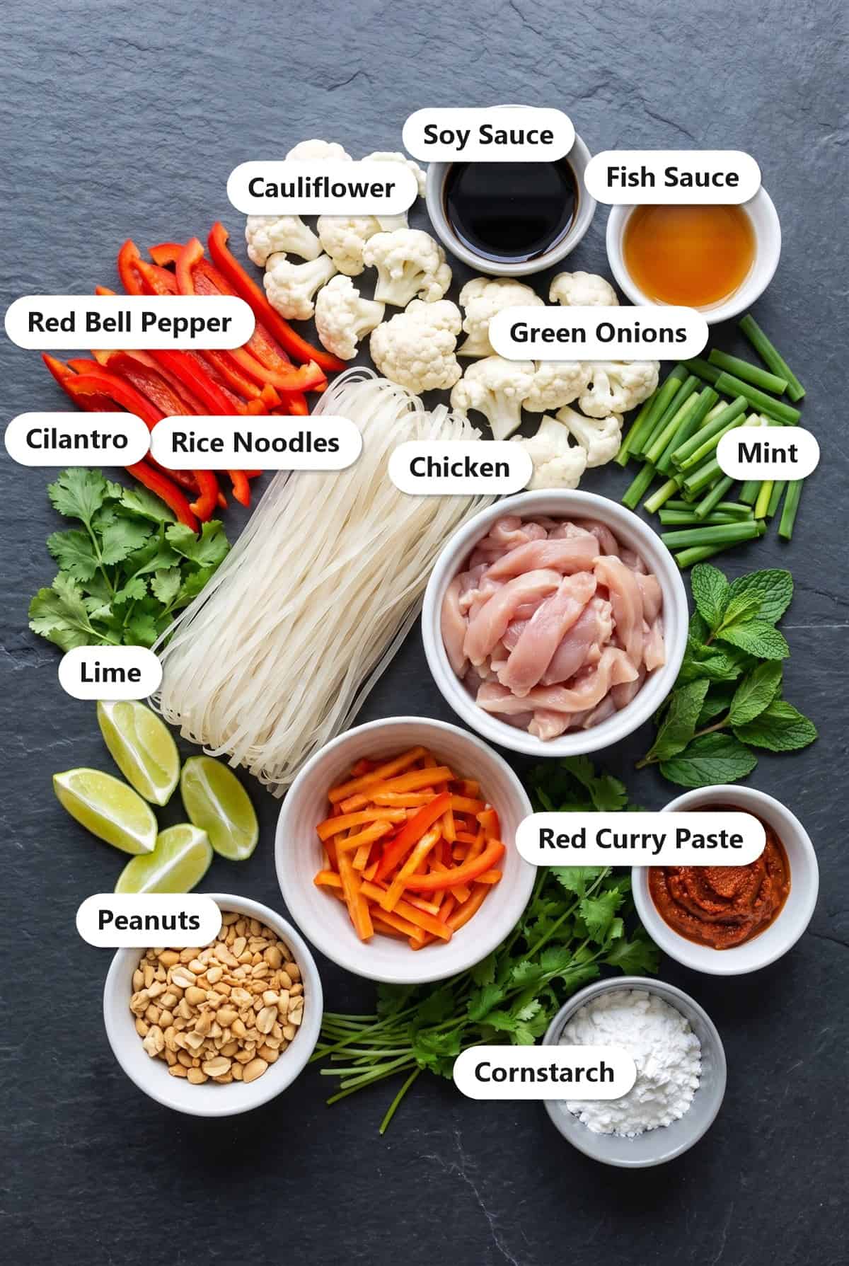 Labeled ingredients for chicken pad thai including rice noodles, chicken thighs, red bell pepper, cauliflower, green onions, peanuts, and sauces.