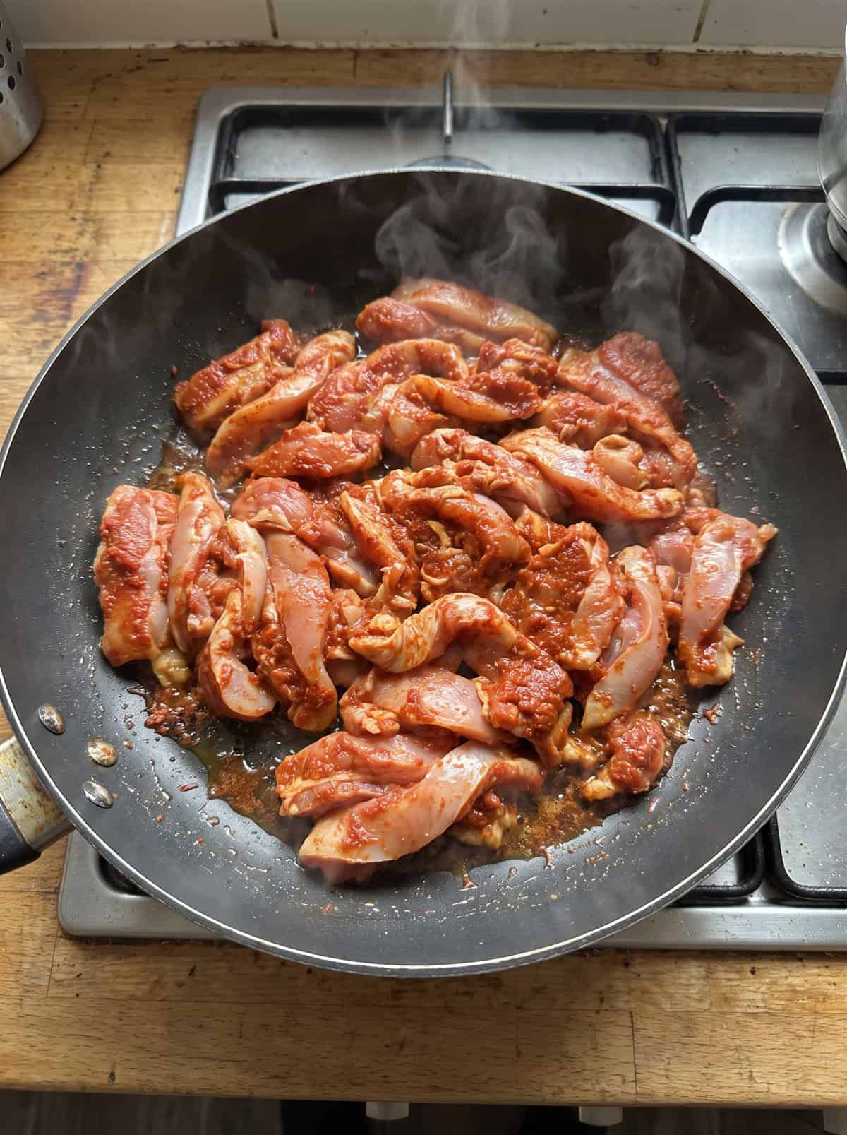 Curry-coated chicken thigh strips searing in a skillet.