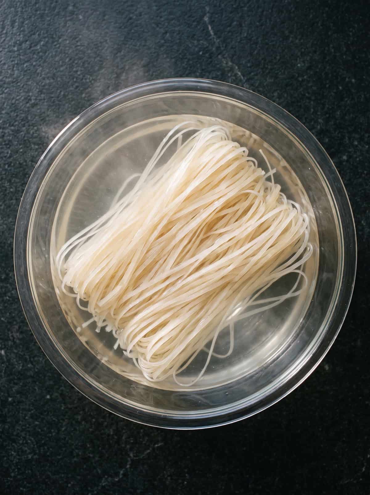 Pad thai rice noodles soaking in a bowl of hot water.