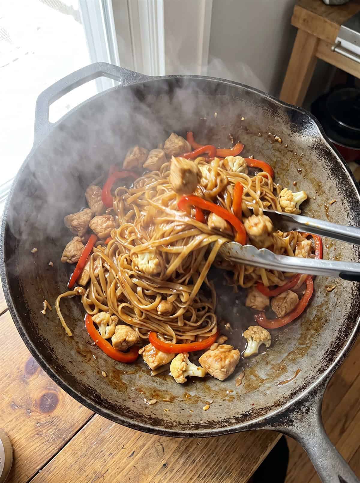 Rice noodles, chicken, and vegetables tossed together with sauce in a skillet.