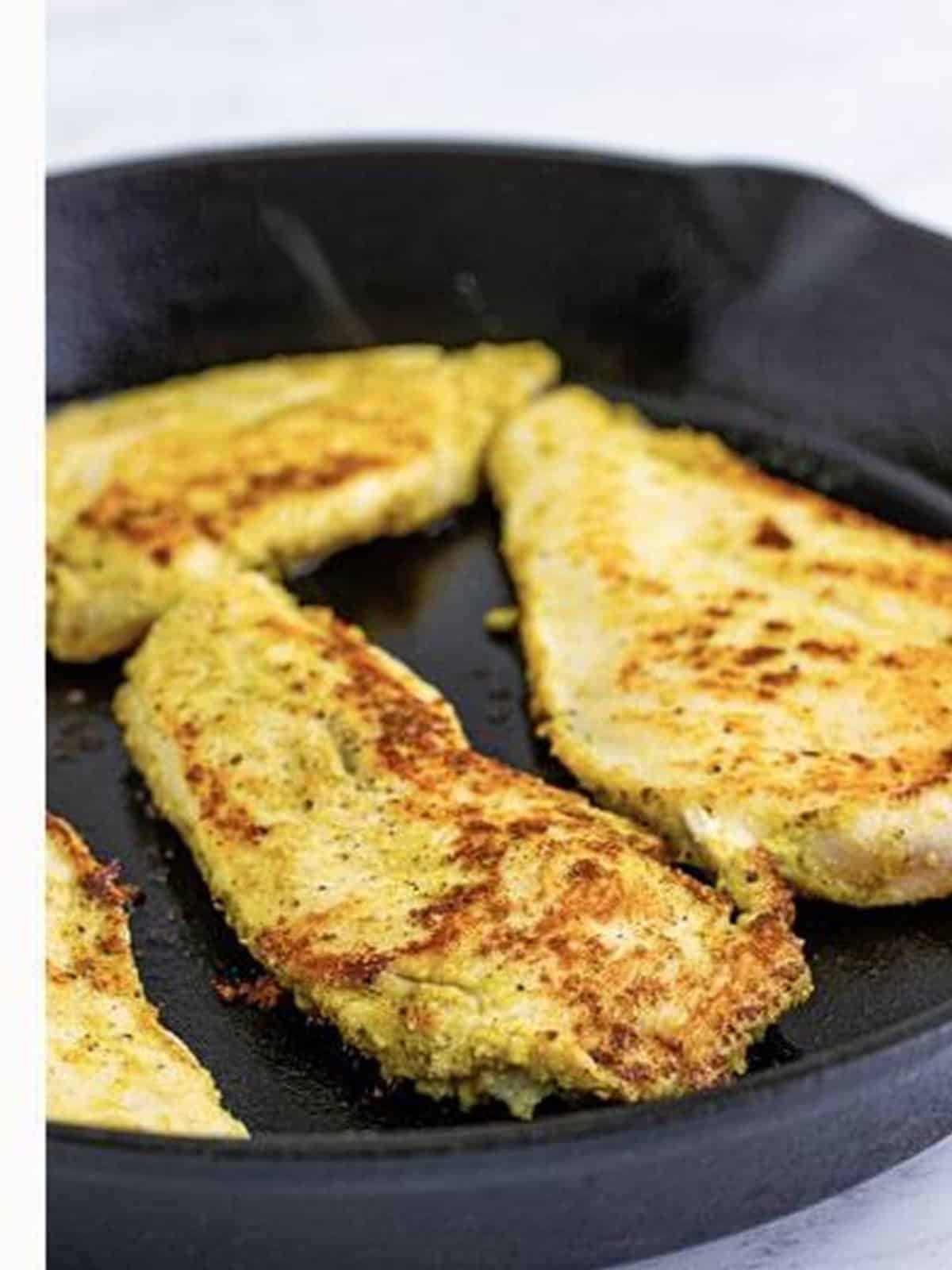 Seasoned chicken breasts searing in a cast iron skillet for chicken pesto sandwiches.