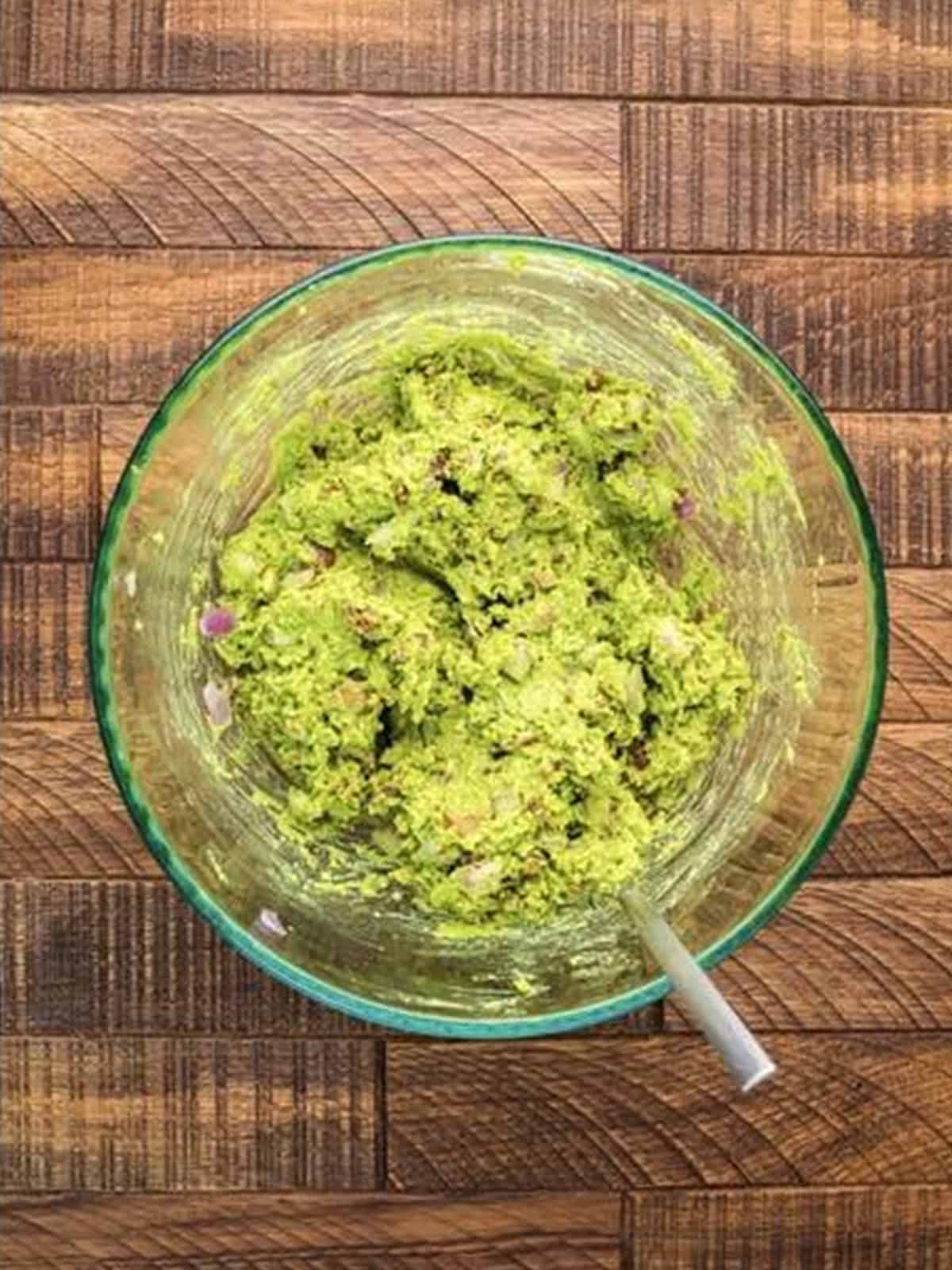 Mashed avocado, bacon, garlic, and onion filling mixed in a glass bowl.