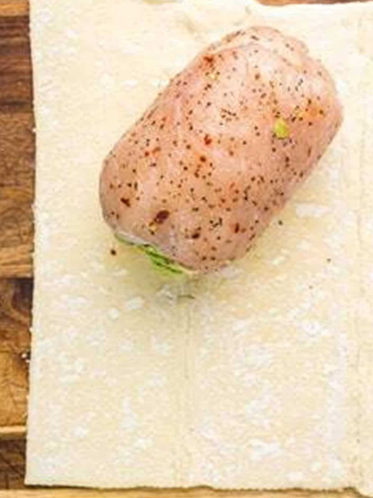 Rolled stuffed chicken placed on a sheet of puff pastry to be wrapped.