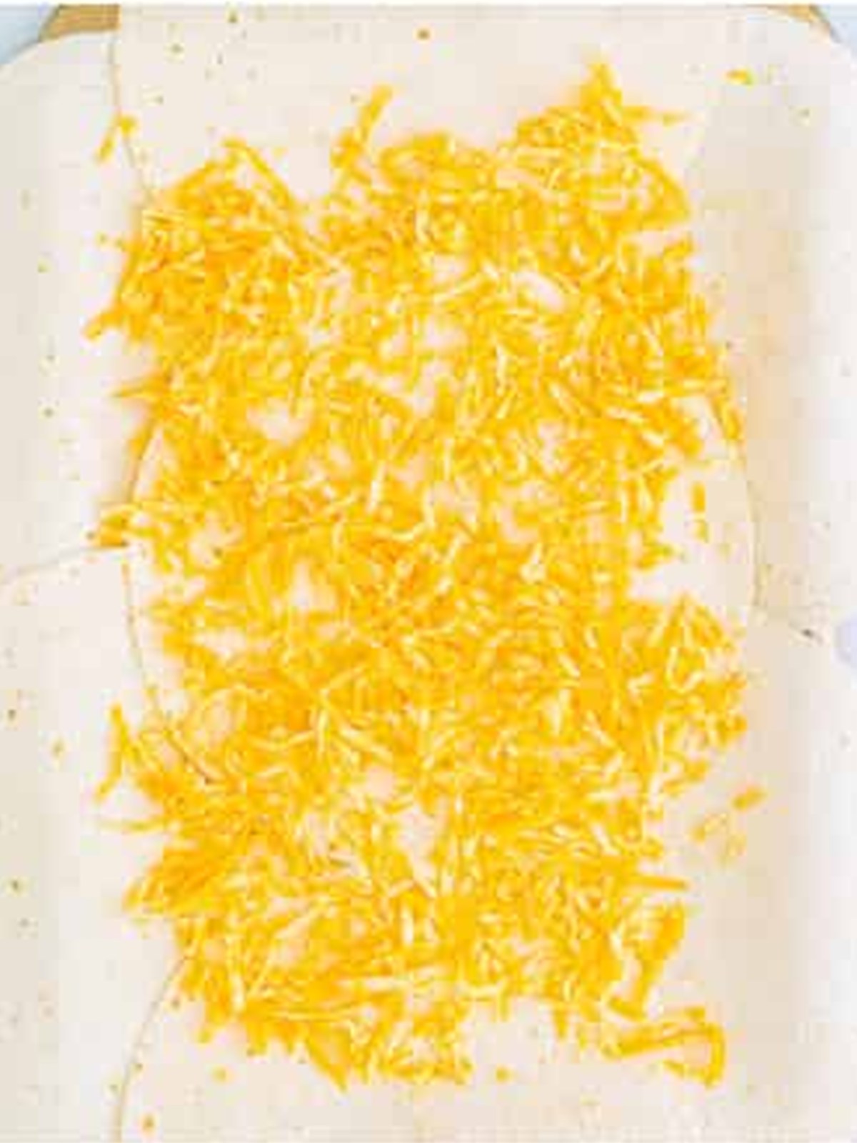 Shredded cheese sprinkled over flour tortillas lining a sheet pan for chicken quesadillas.