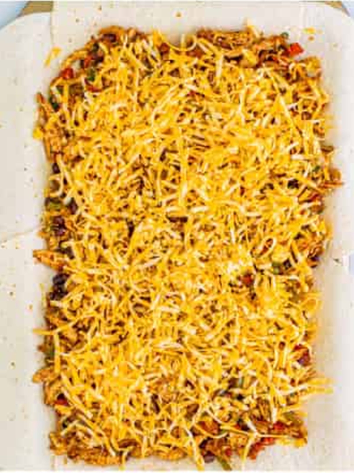 A second layer of shredded cheese over the filling on the sheet pan.