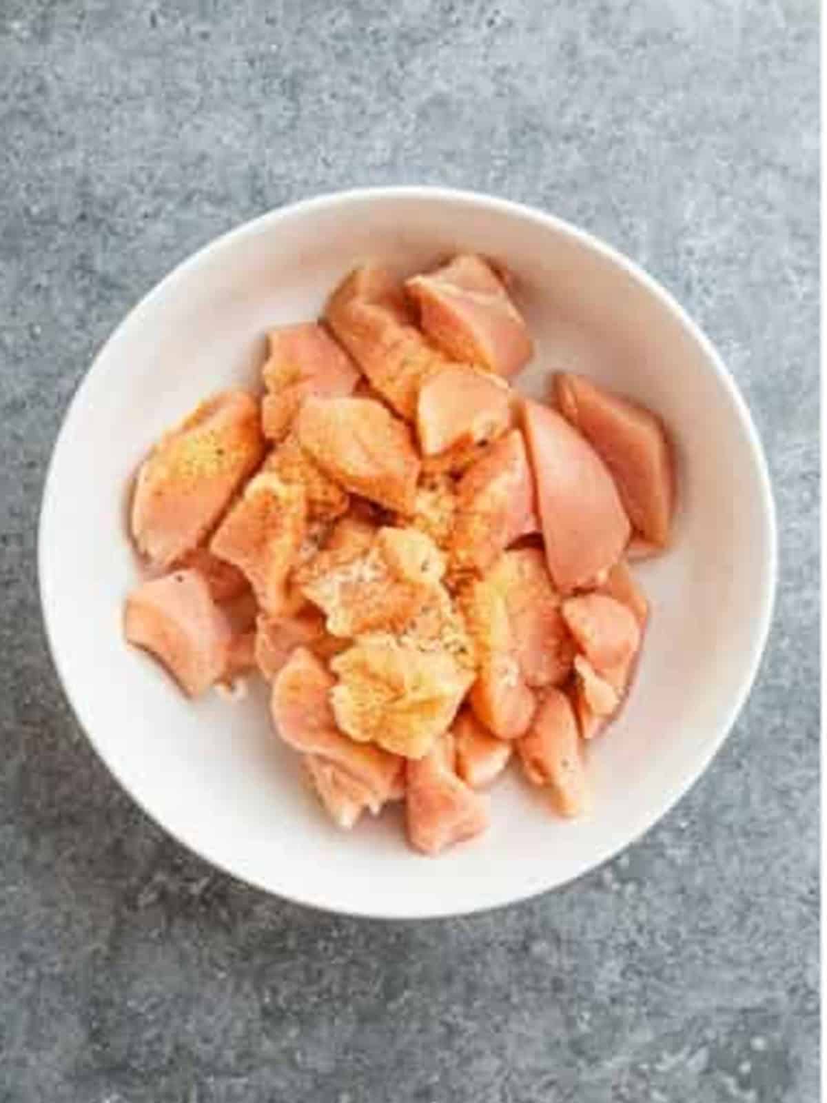 Bite-sized chicken breast pieces seasoned with garlic powder, salt, and pepper in a bowl.