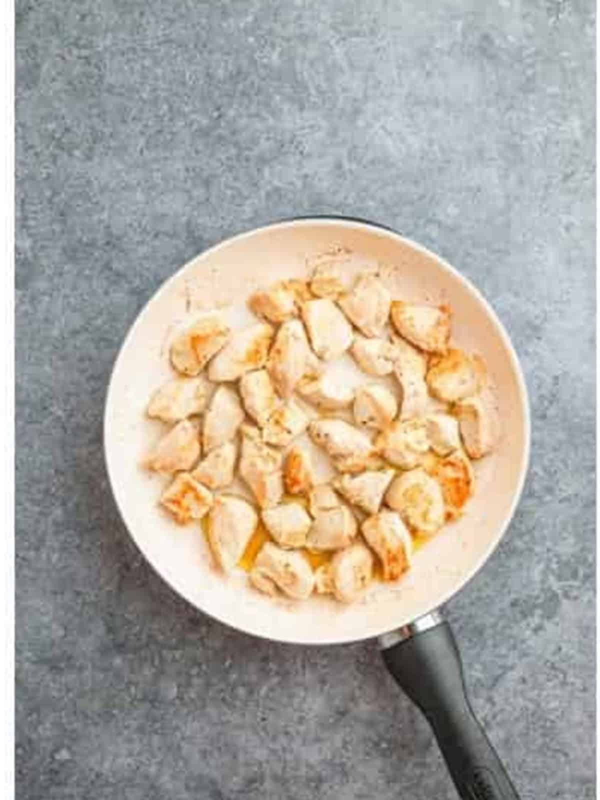 Chicken pieces seared until golden brown in a skillet.