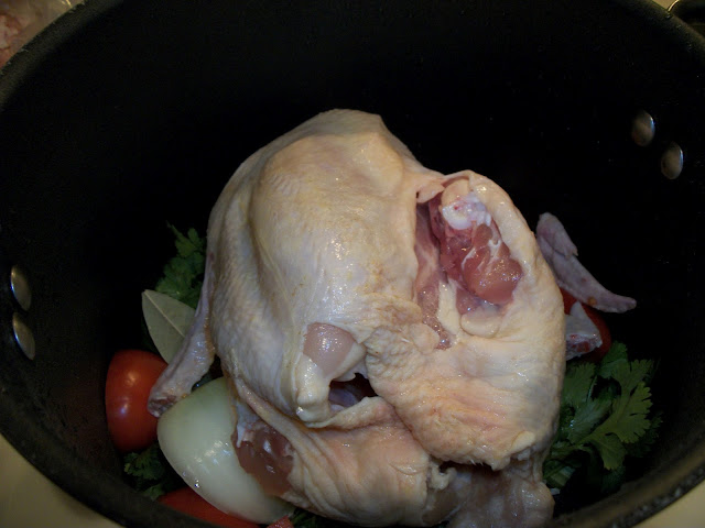 A whole chicken simmering with tomatoes, onion, lime, and cilantro for tamale filling.