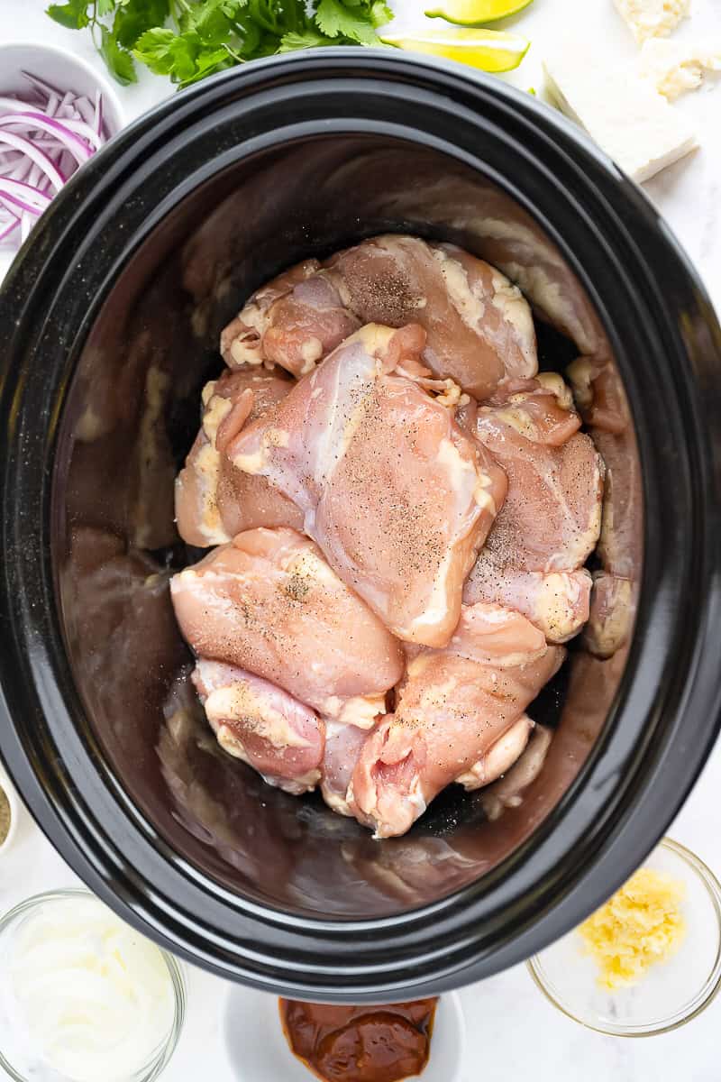 Boneless chicken thighs seasoned with salt and pepper in the slow cooker for chicken tinga.