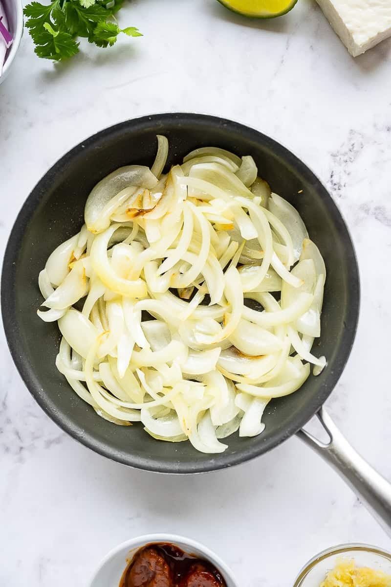 Sliced onions sauteed in a skillet until soft and translucent for chicken tinga.