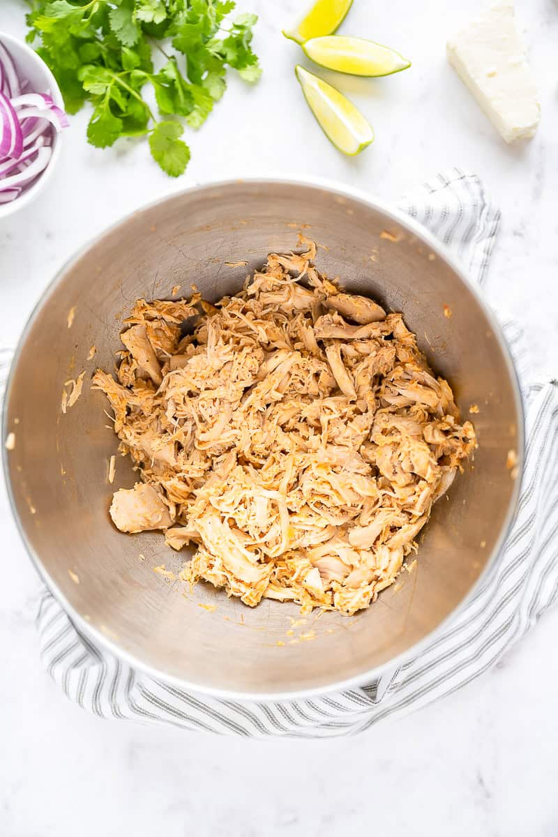 Cooked chicken thighs shredded with two forks in a bowl for chicken tinga.