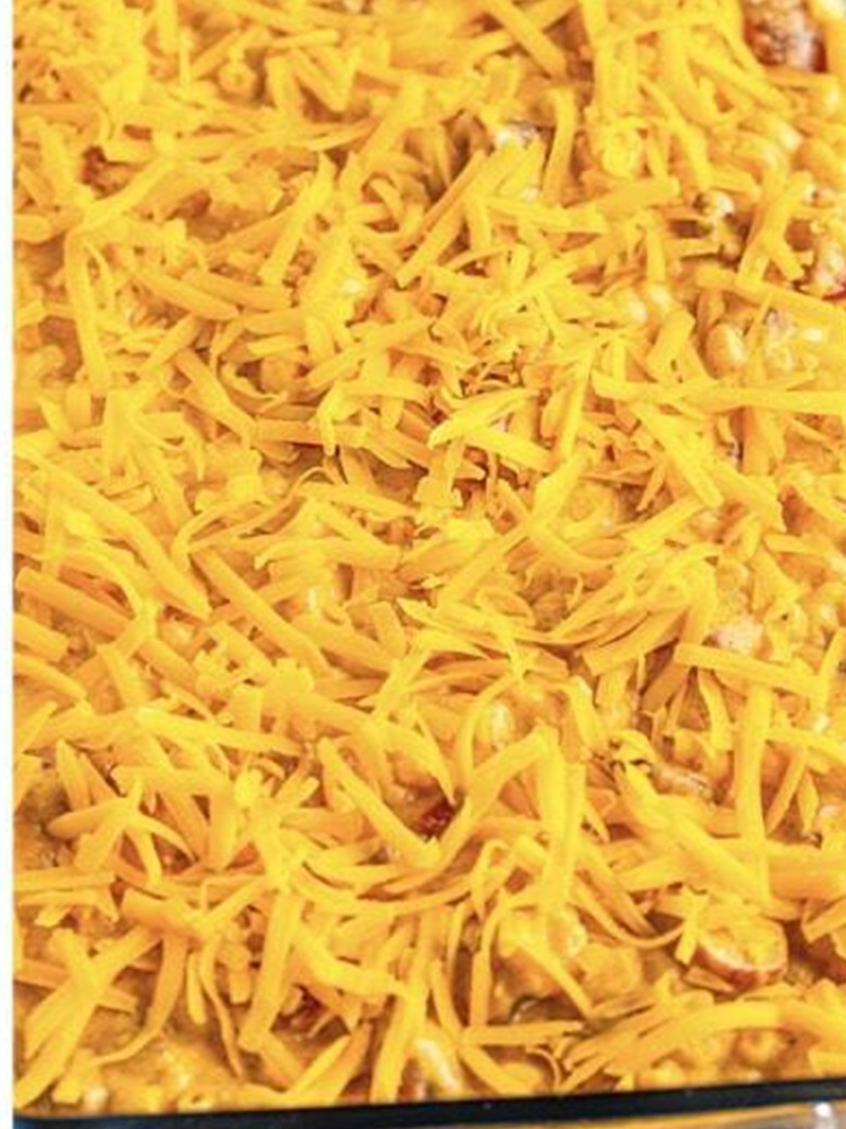 Chili cheese dog mac and cheese in a baking dish topped with shredded cheddar.