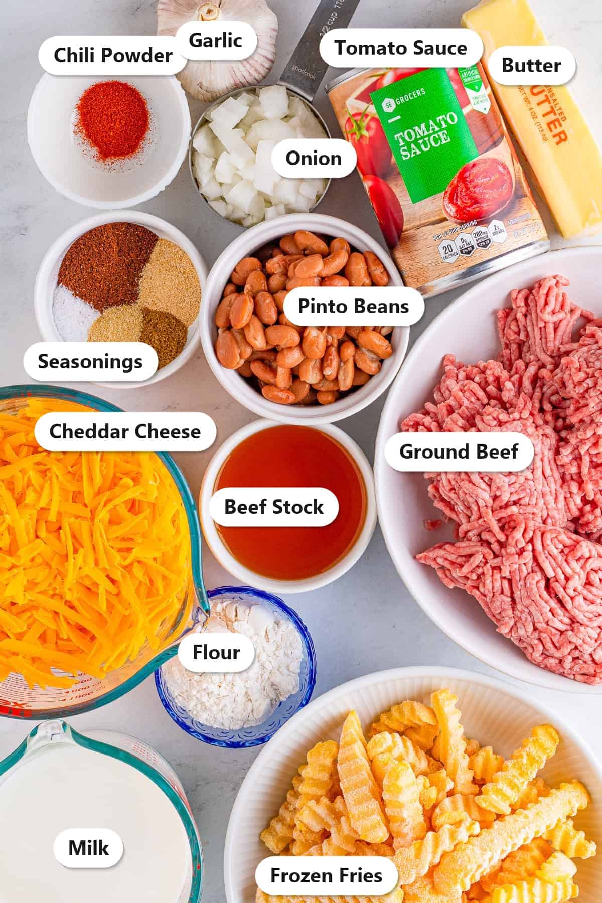 Labeled ingredients to make chili cheese fries including frozen fries, ground beef, pinto beans, cheddar cheese, tomato sauce, beef stock, and seasonings.