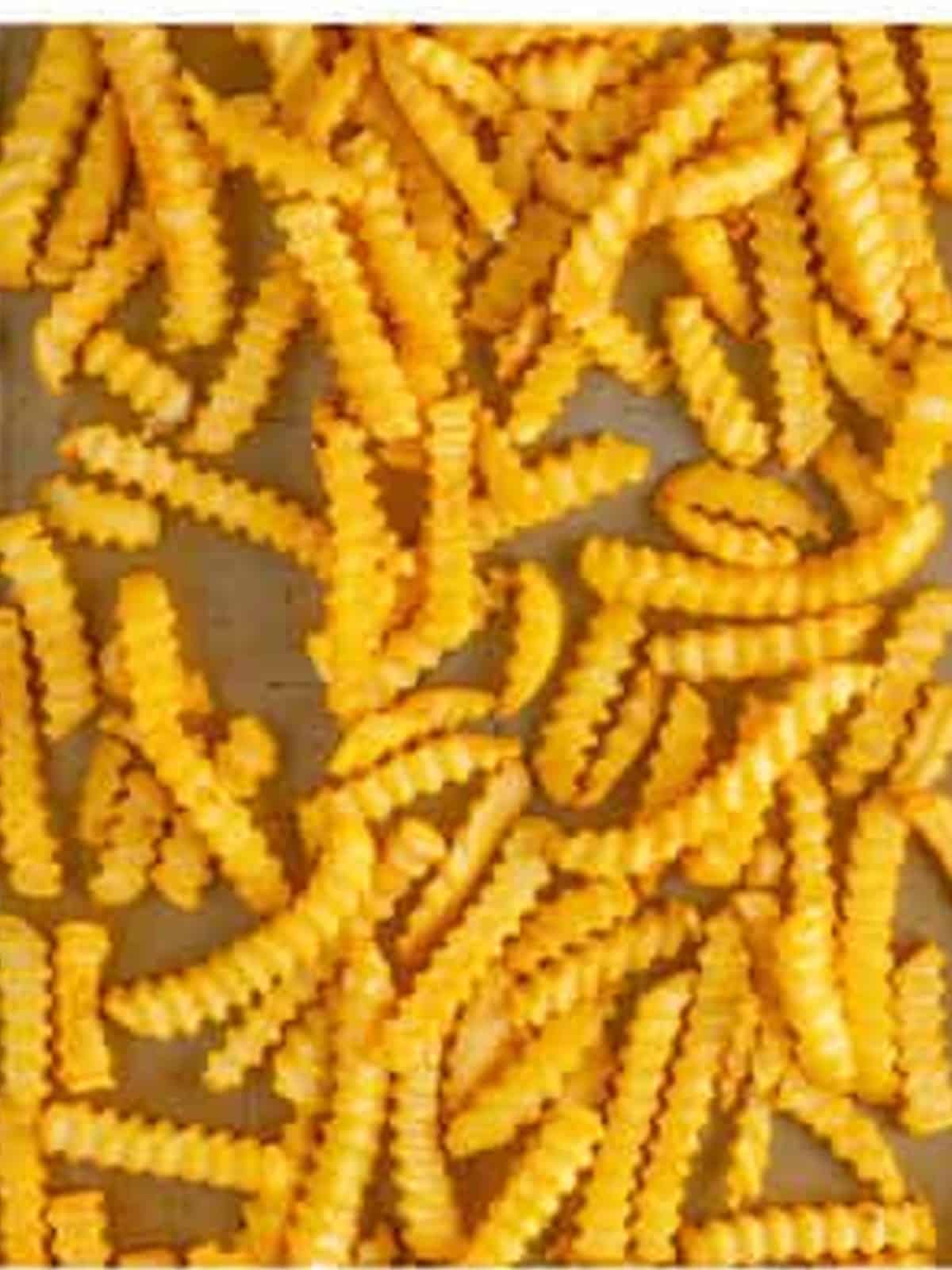 Frozen crinkle cut fries spread on a sheet tray to bake for chili cheese fries.