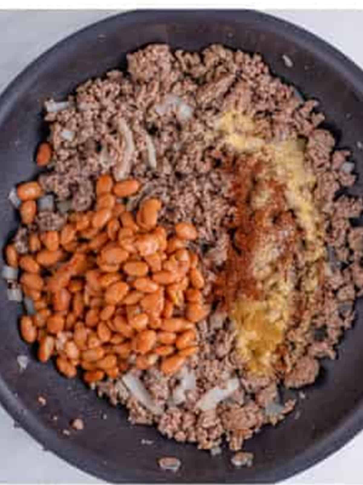 Browned ground beef with pinto beans and spices in a skillet for the chili.