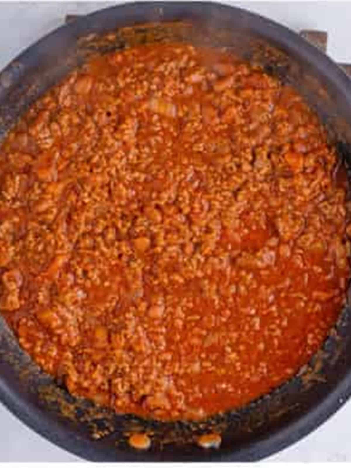Chili simmered with tomato sauce and beef stock in a skillet.