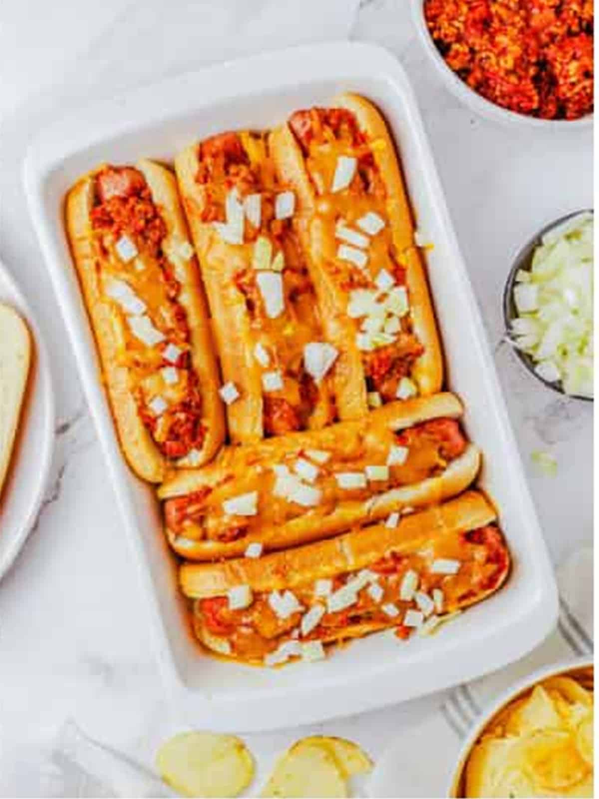 Baked chili dogs topped with melted cheese and chopped onion.