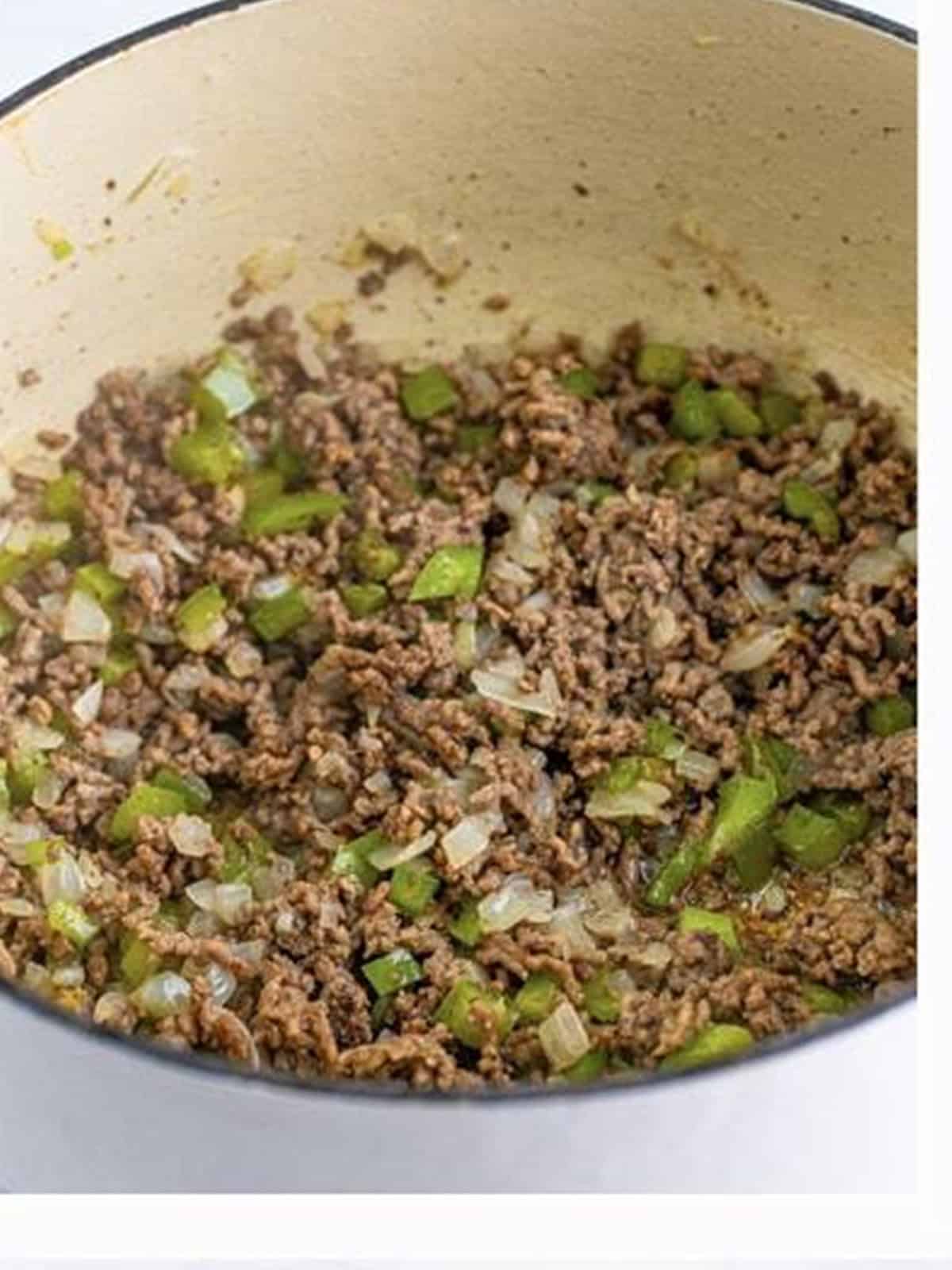 Ground beef browning with onion and green bell pepper in a Dutch oven for chili mac.