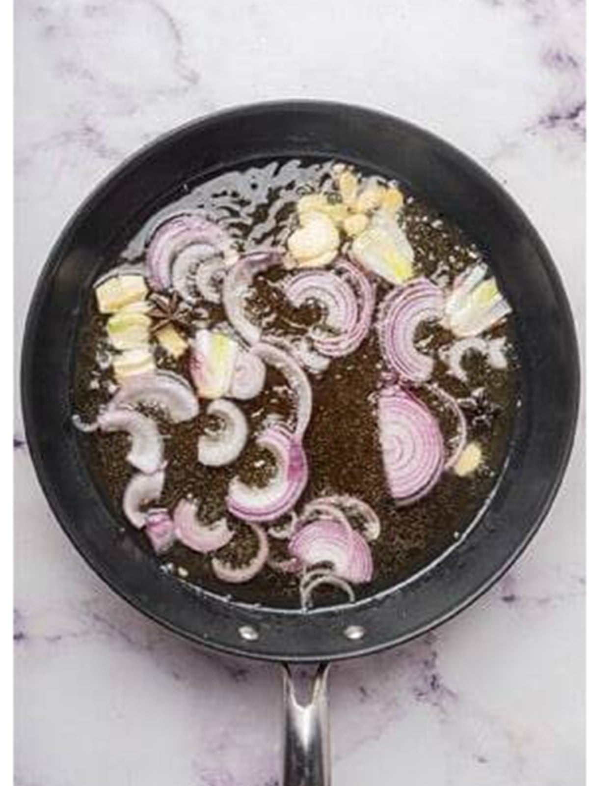Sliced ginger, garlic, and onion frying in hot oil in a skillet for chili oil.