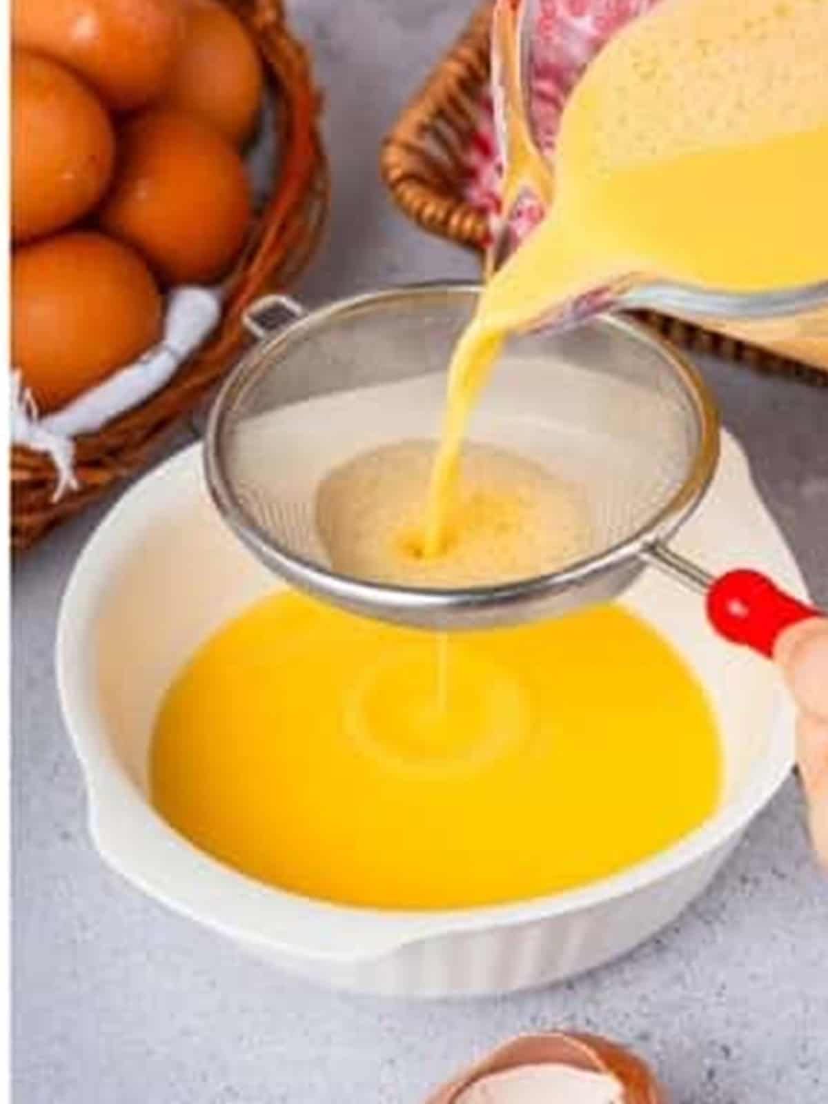 The egg mixture being strained through a fine sieve into a shallow bowl.