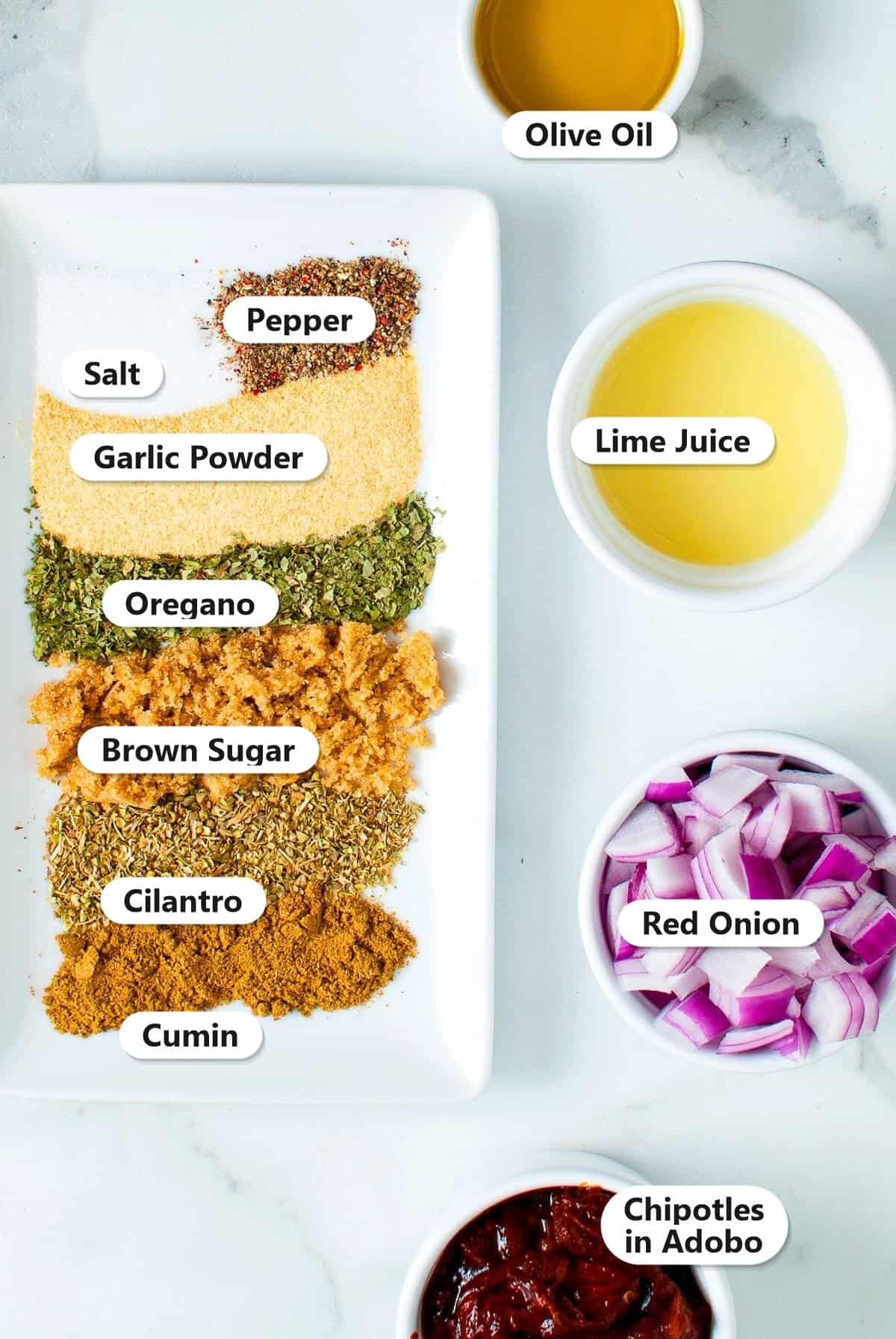Labeled chipotle chicken marinade ingredients including chipotles in adobo, olive oil, lime juice, red onion, brown sugar, garlic powder, oregano, cilantro, cumin, salt, and pepper.