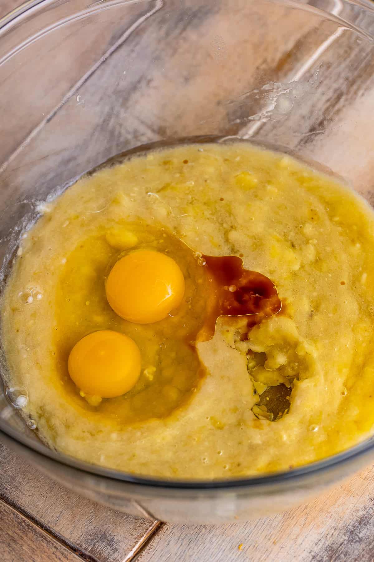 Mashed bananas, eggs, oil, and vanilla whisked in a glass bowl for chocolate banana muffins.