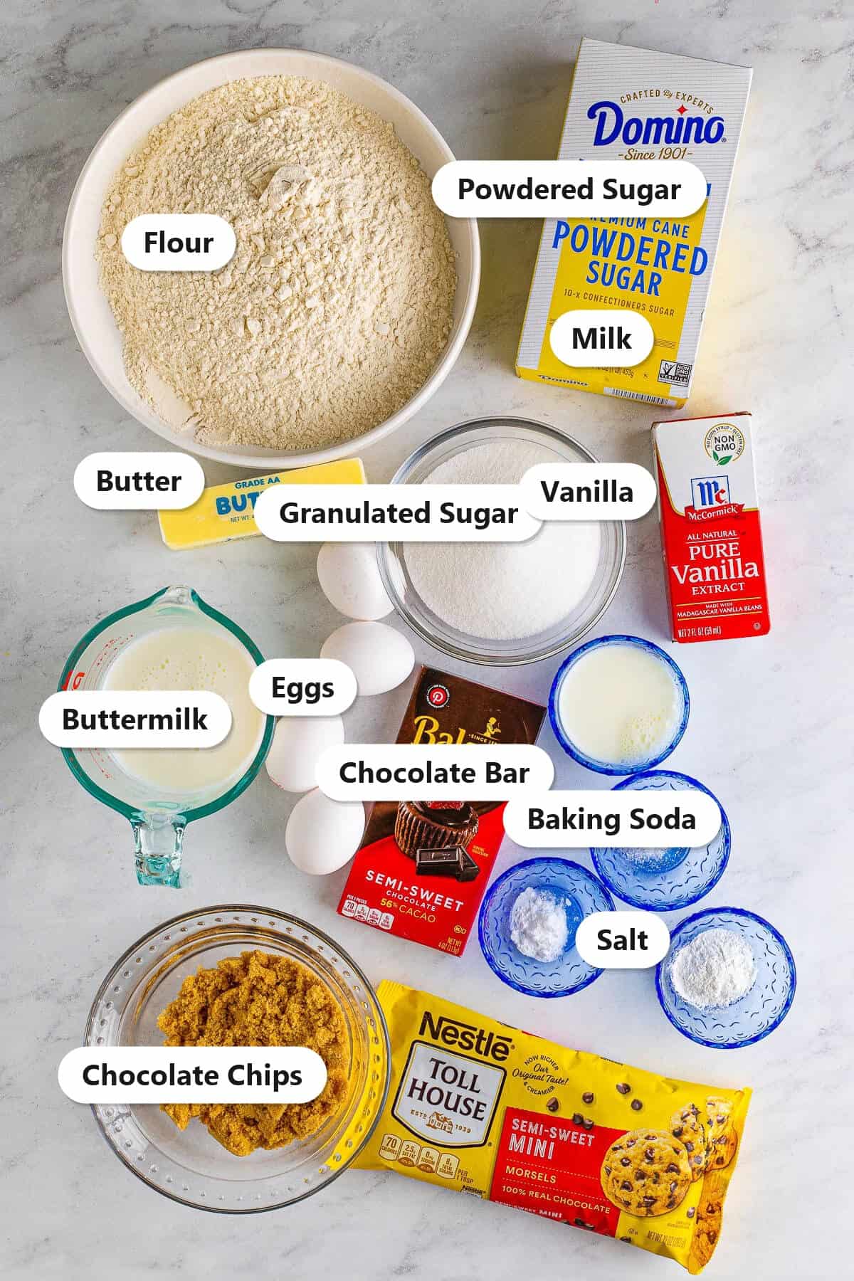 Labeled ingredients for chocolate chip cake including flour, butter, sugar, eggs, buttermilk, mini chocolate chips, and powdered sugar.