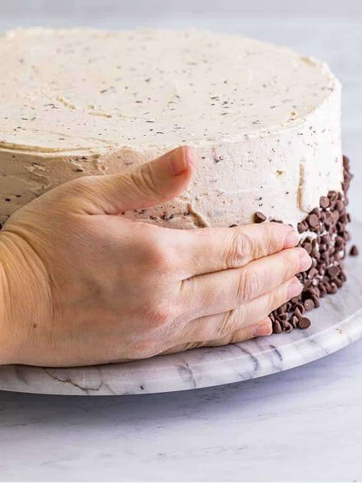 Frosting a chocolate chip cake and pressing mini chocolate chips around the base.