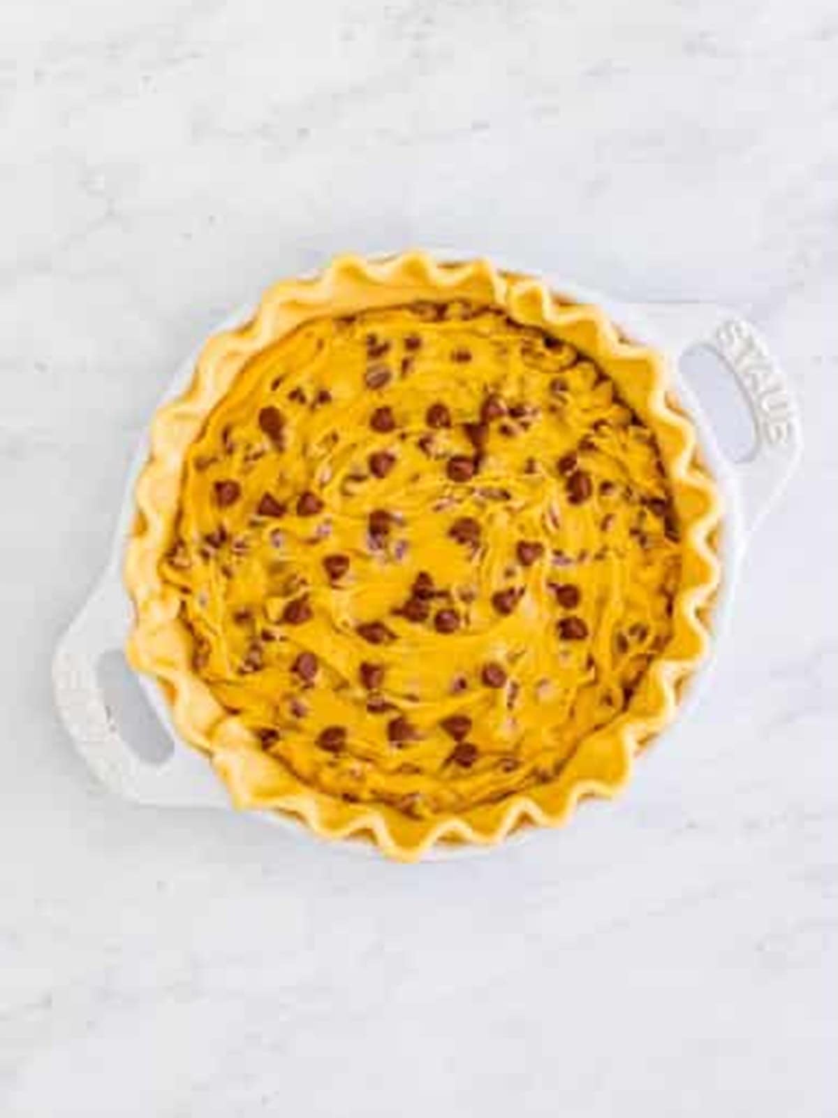 Chocolate chip cookie batter spread into a pie crust before baking.