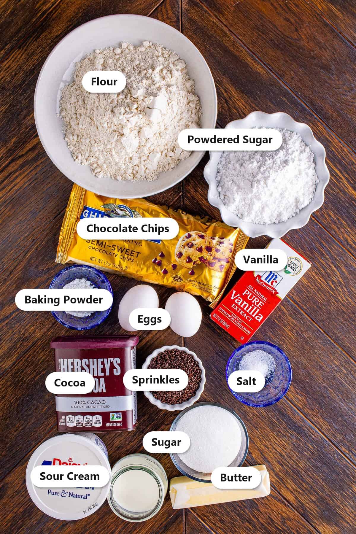 Labeled ingredients to make baked chocolate chip donuts including flour, sugar, chocolate chips, cocoa, eggs, sour cream, butter, and sprinkles.