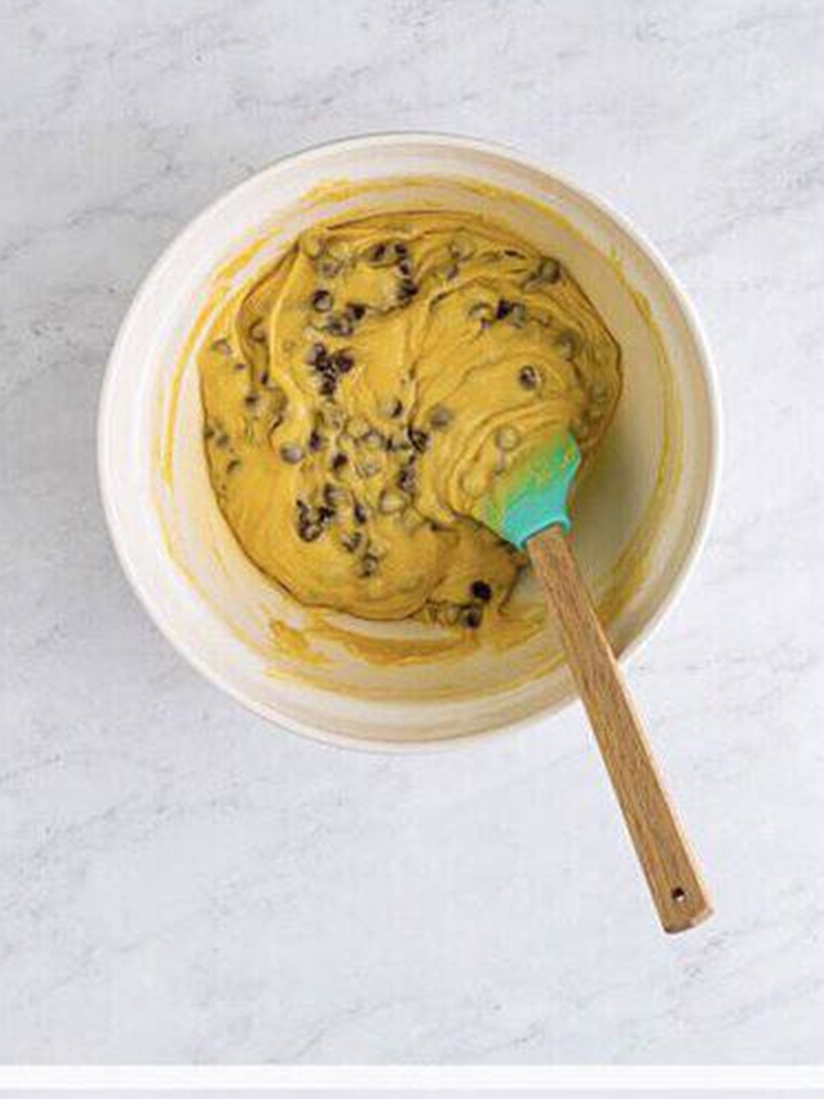 Chocolate chips folded into the smooth muffin batter with a spatula.