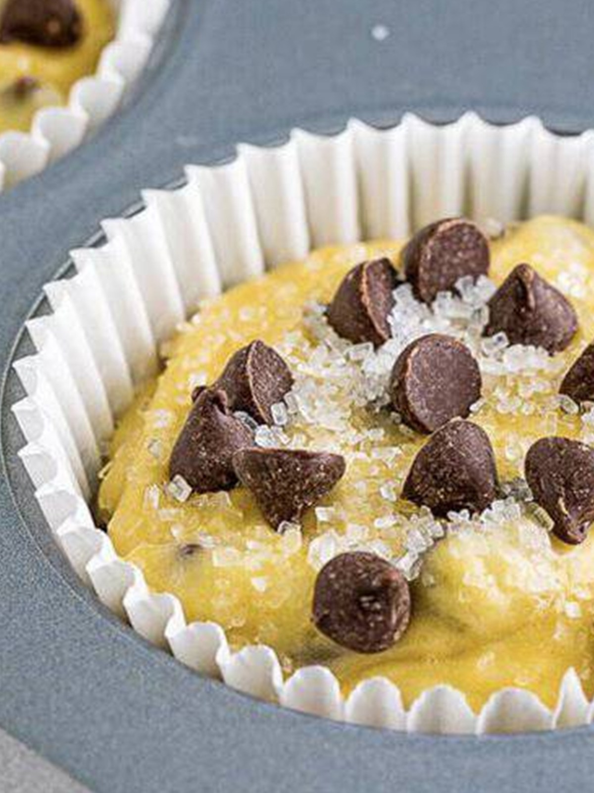 Chocolate chip muffin batter divided into a lined muffin tin and topped with extra chocolate chips.